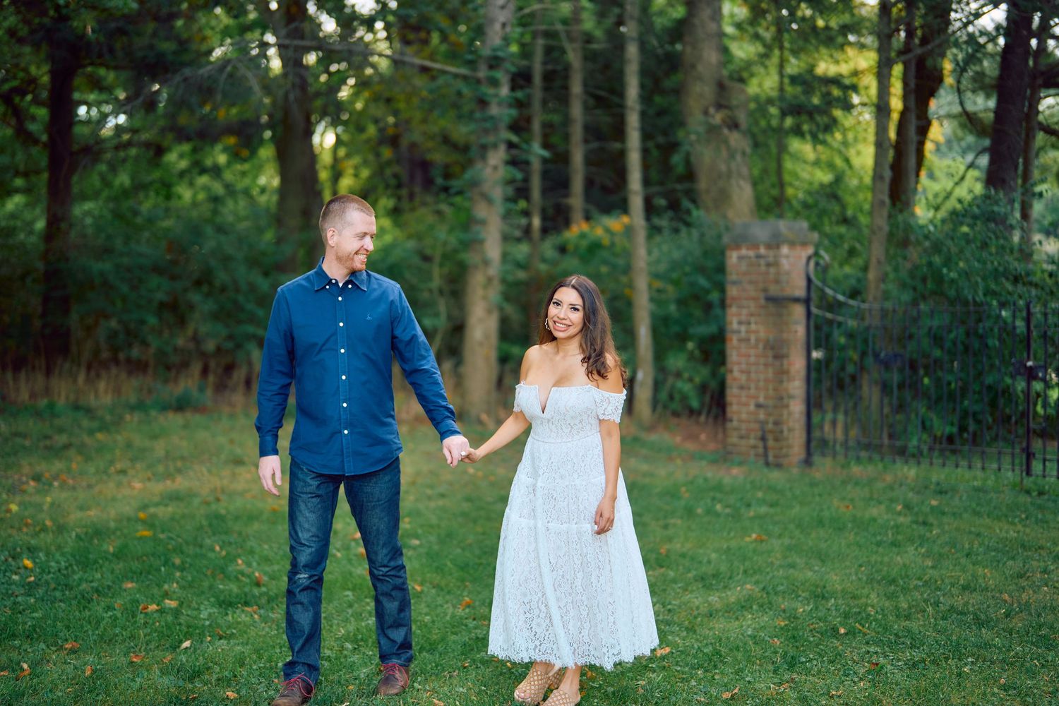 A couple stands together holding hands in a lush garden setting wearing blue and white attire.