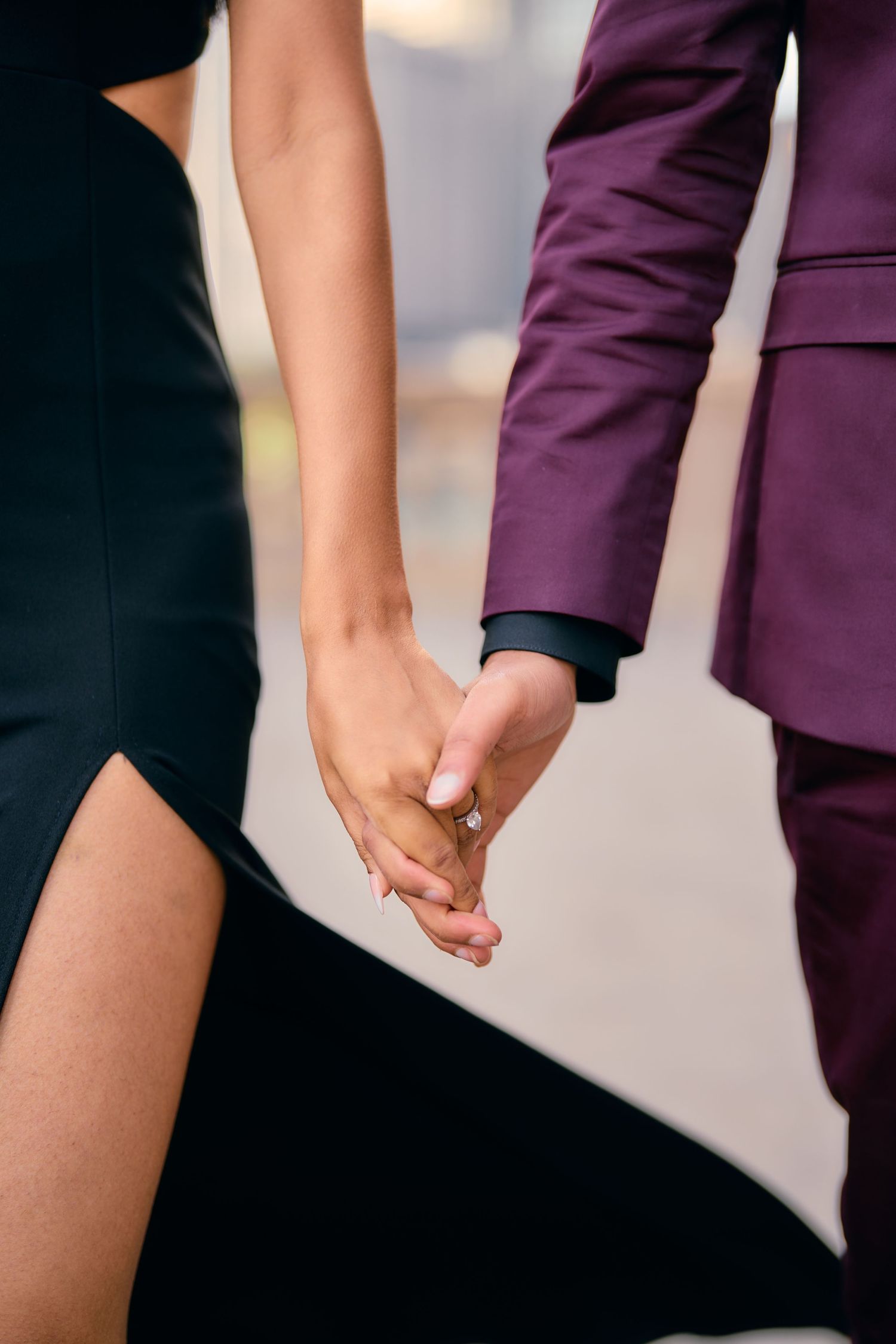 Close-up of two people holding hands, one wearing a black dress and the other in a purple suit.