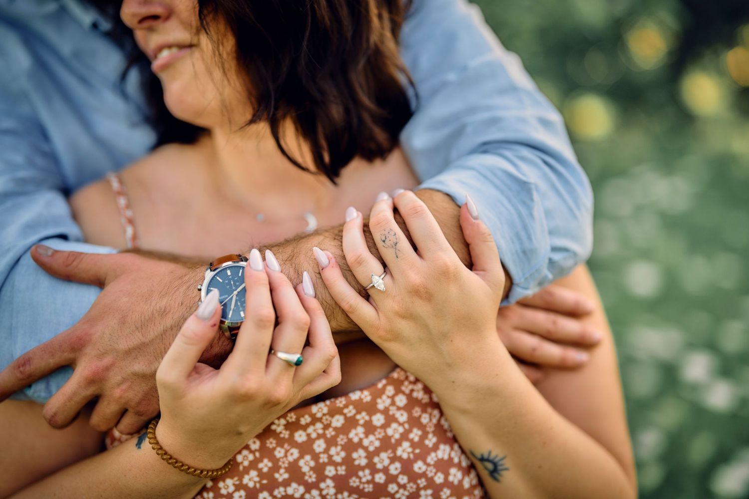 Close-up of hands embracing tenderly in a sunny garden setting with a floral print dress visible.