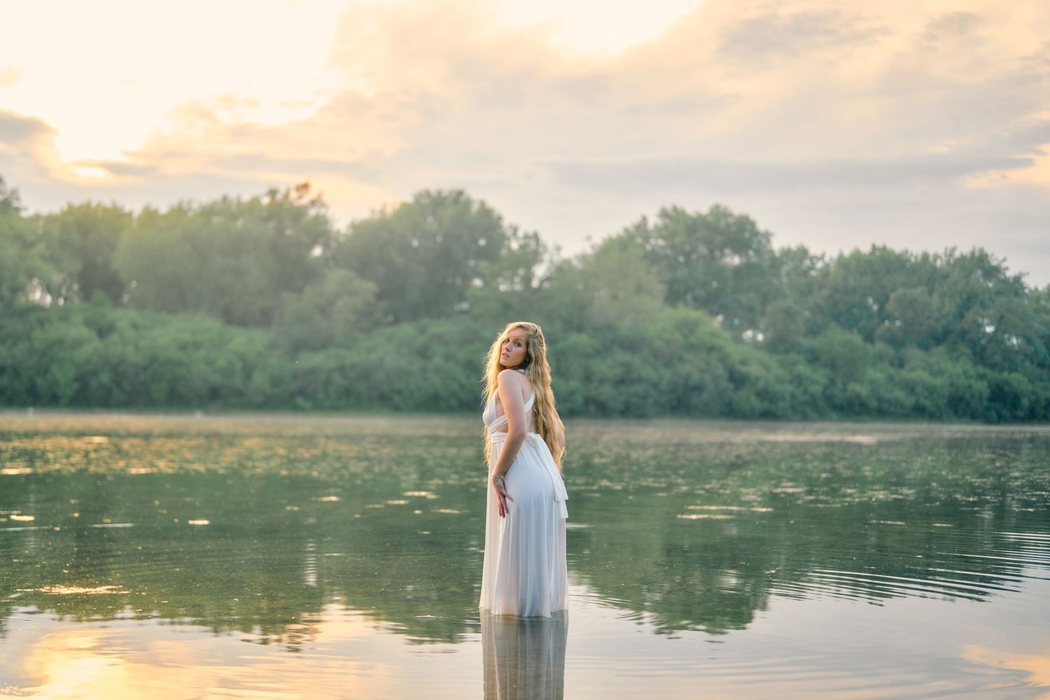 Woman in white dress standing in lake during sunset.