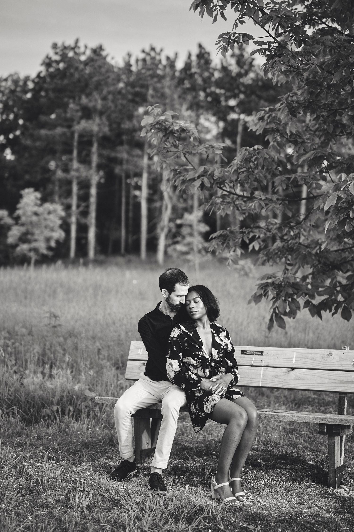 Romantic black and white photo of a couple sitting together on a wooden bench in a peaceful outdoor setting with trees.