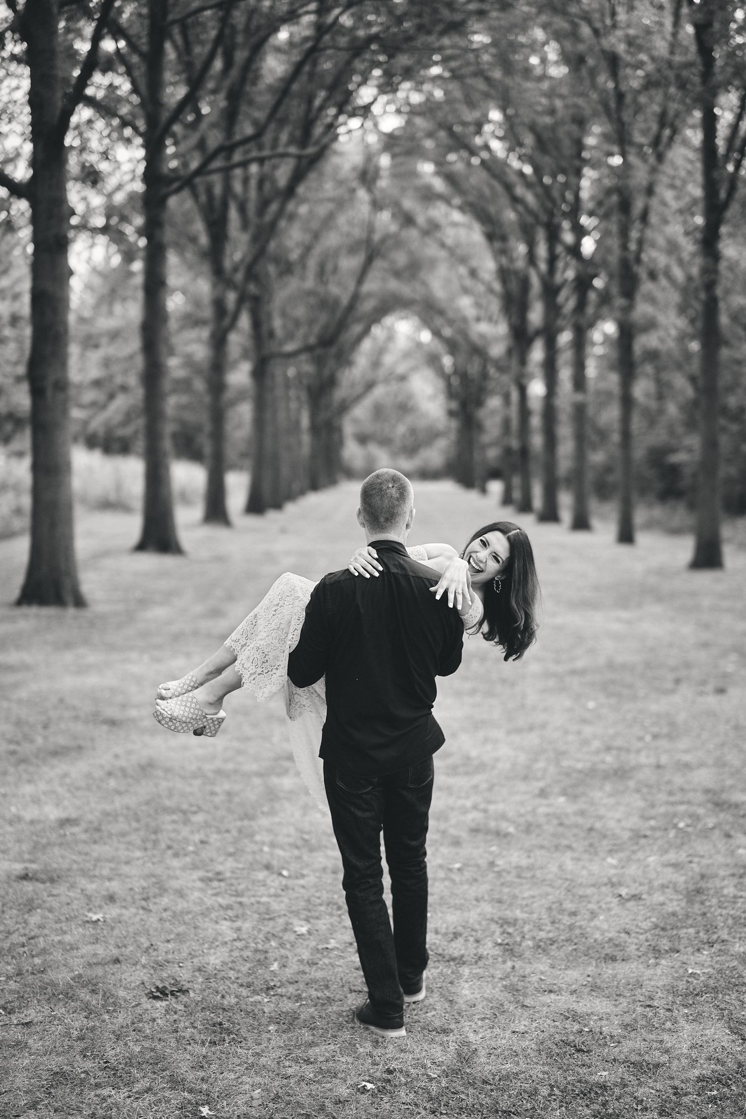 A romantic black and white photo of a couple embracing in a tree-lined path, creating a natural tunnel effect.
