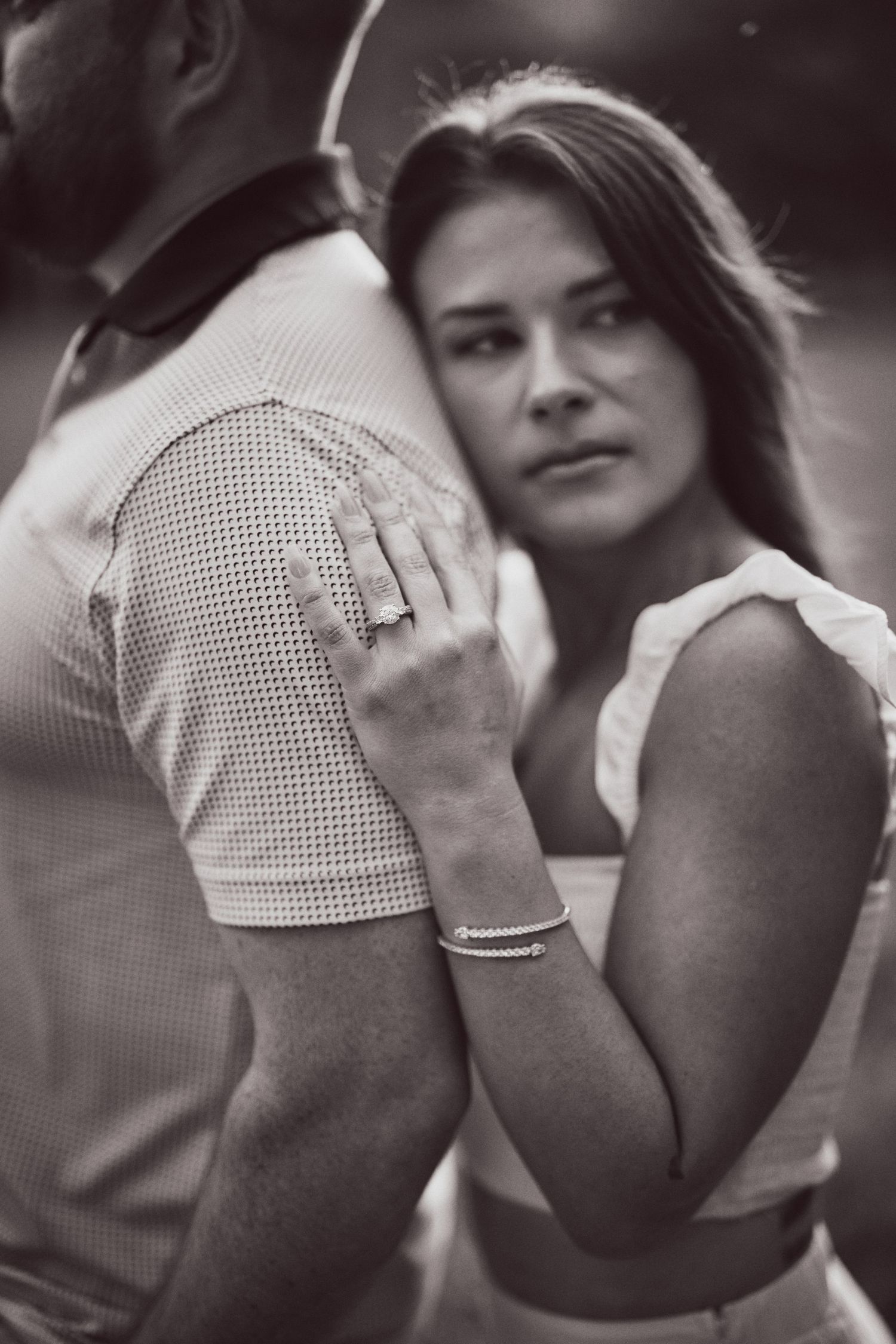 Black and white romantic portrait of an intimate couple embracing, with focus on her hands against his patterned shirt.