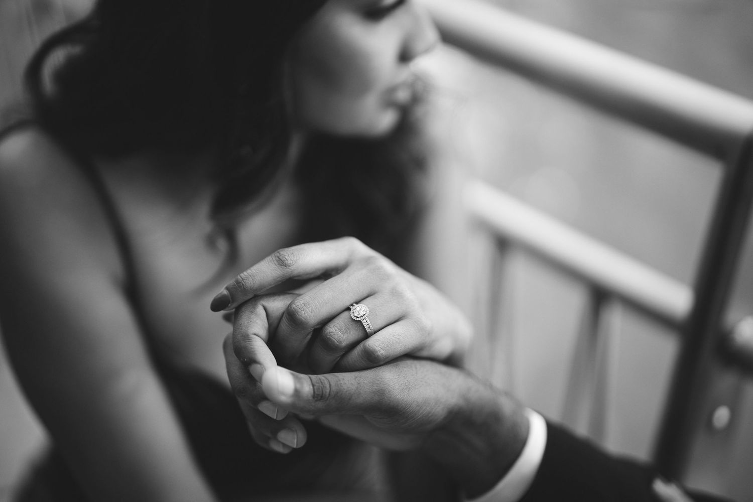 Close-up black and white shot of hands with a ring in soft focus and dramatic lighting.