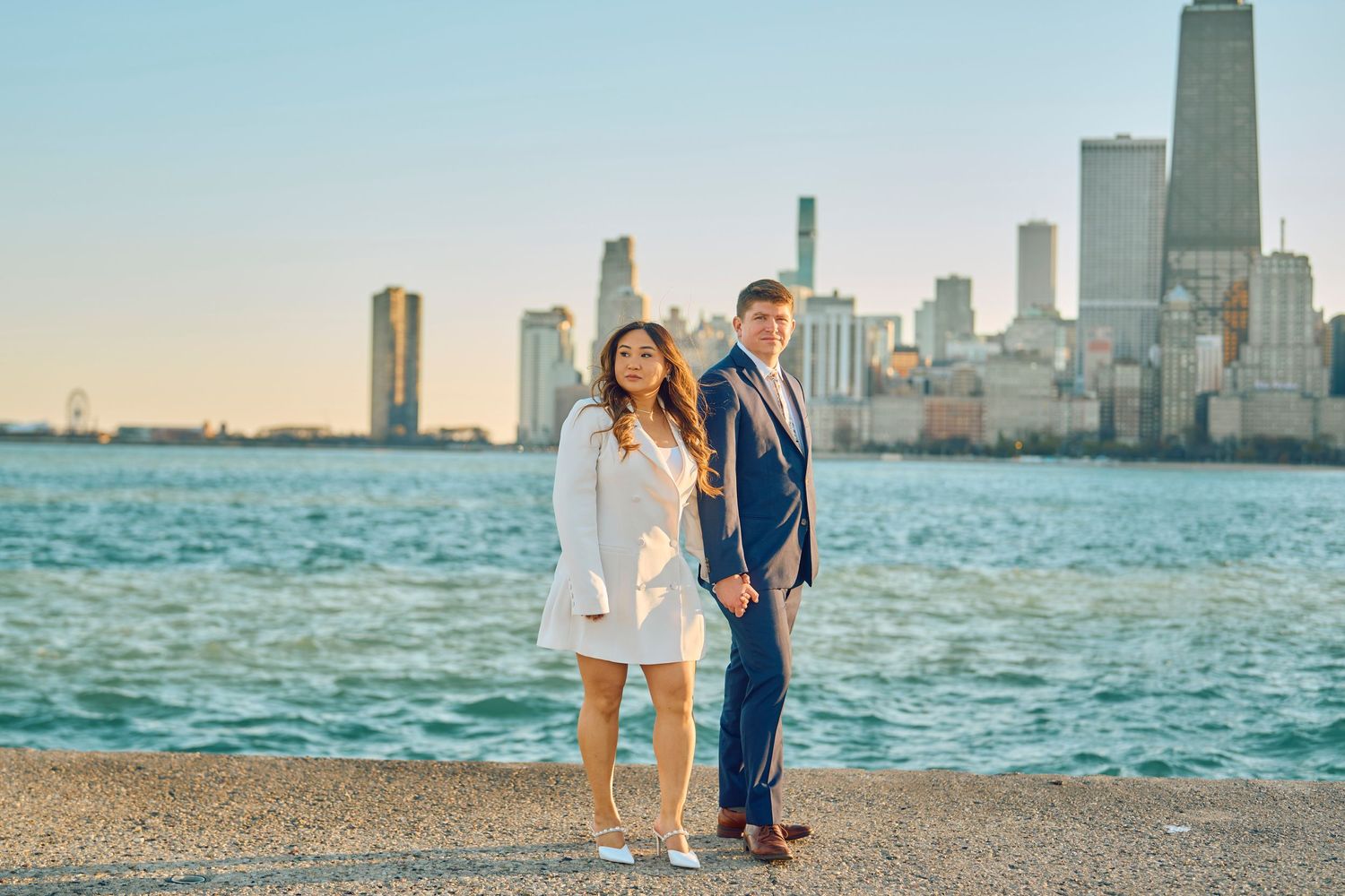 Couple poses together by Lake Michigan with Chicago's stunning skyline at sunset.