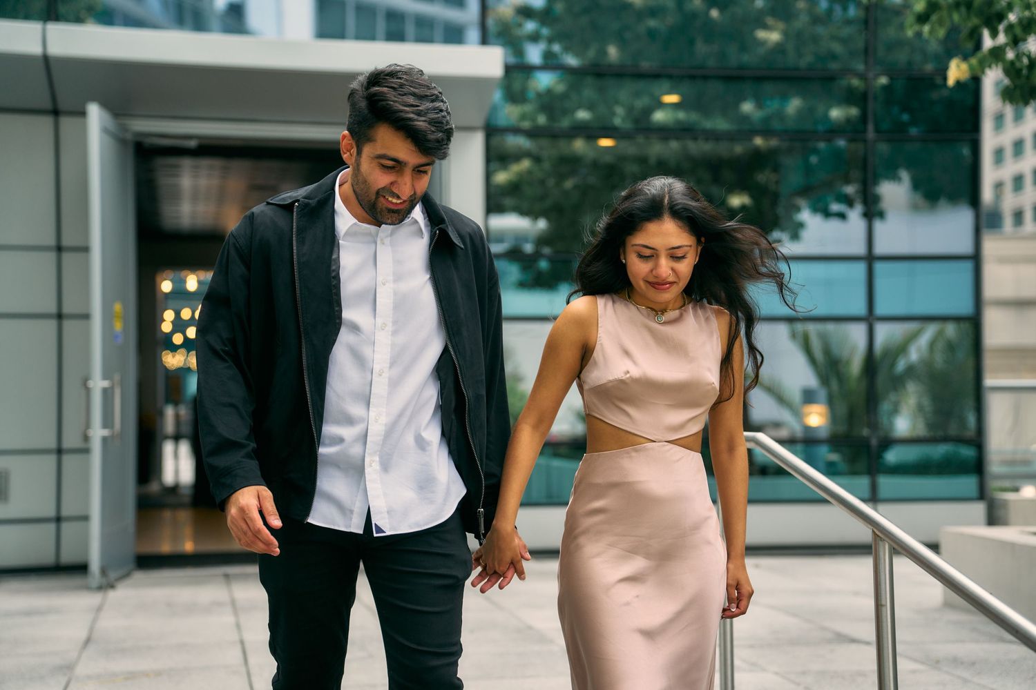 A couple walking together on a modern urban pathway wearing elegant attire.