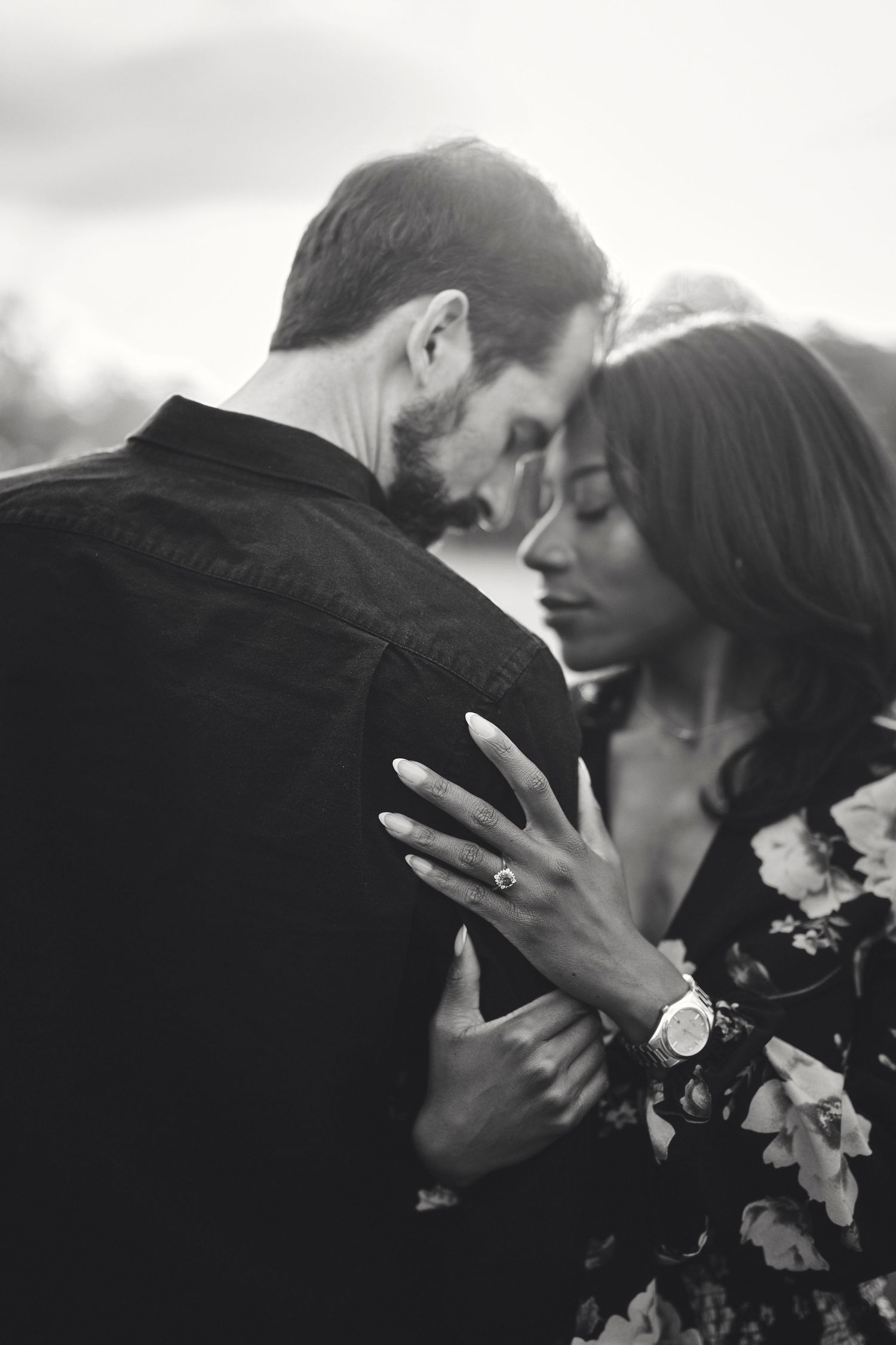 A romantic black and white portrait of a couple in an intimate embrace with the woman wearing a floral dress.