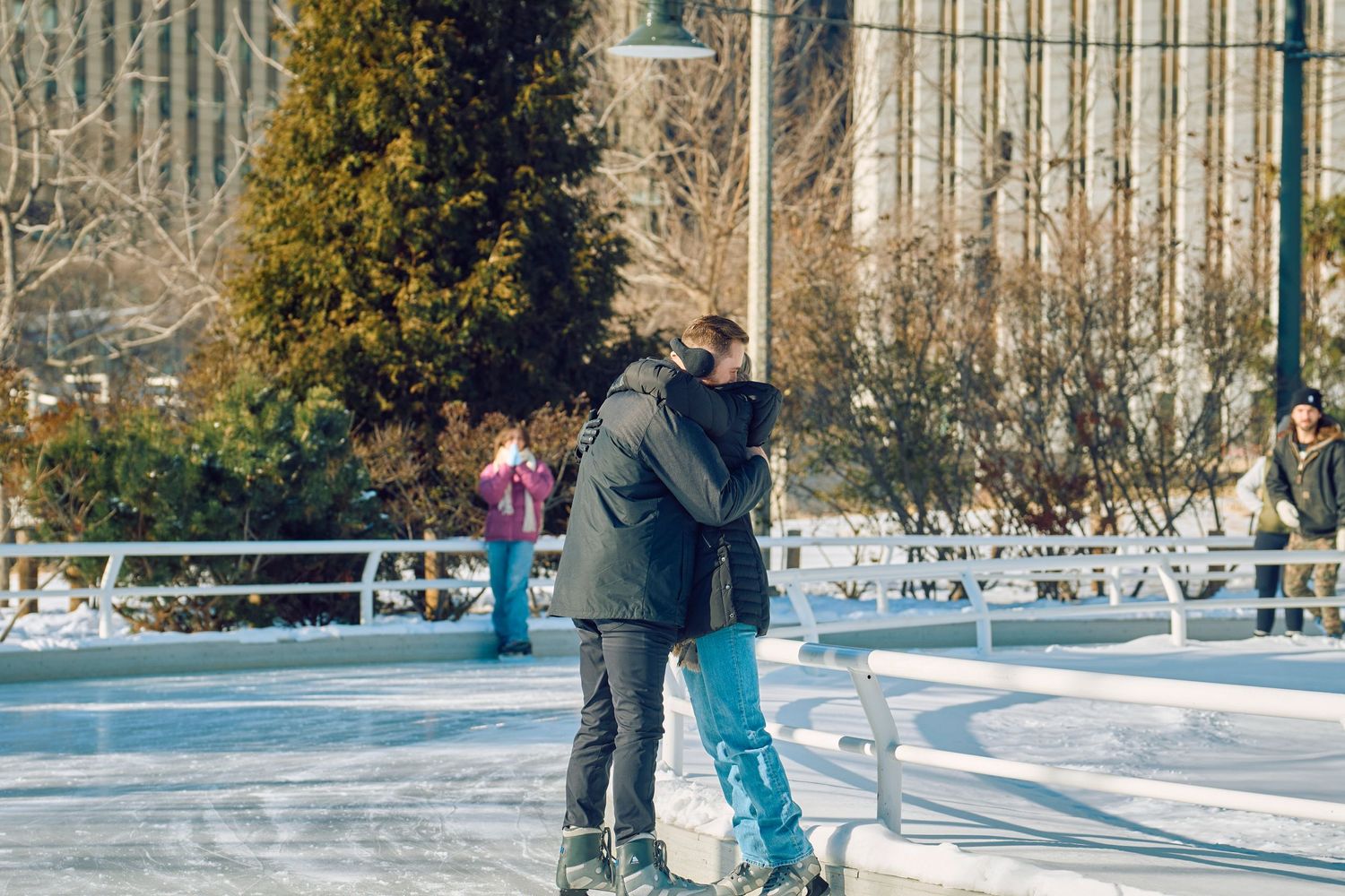 Two people ice skating together on an outdoor rink surrounded by winter scenery.