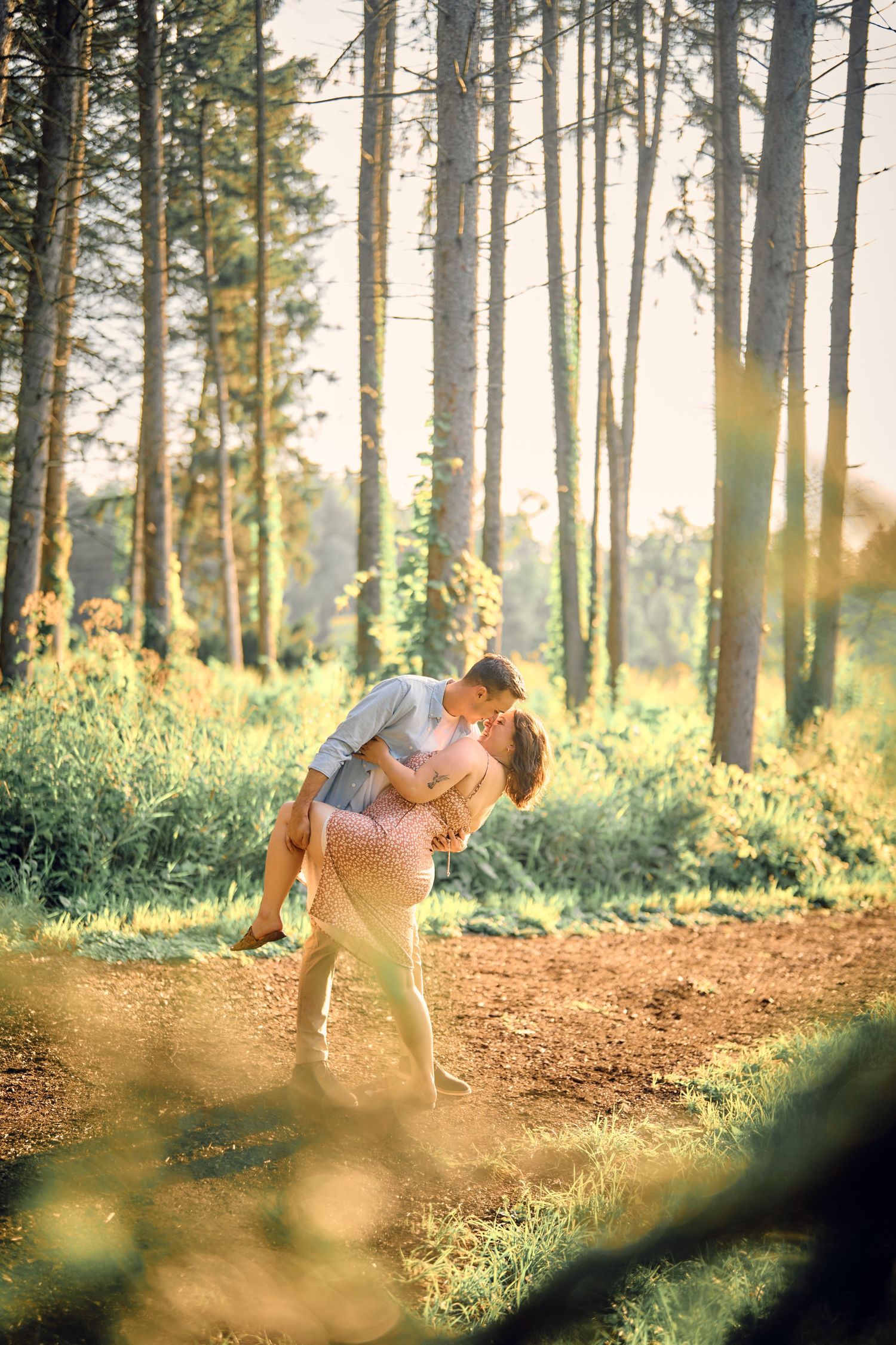 A romantic couple shares a tender moment on a sunlit forest trail during golden hour.
