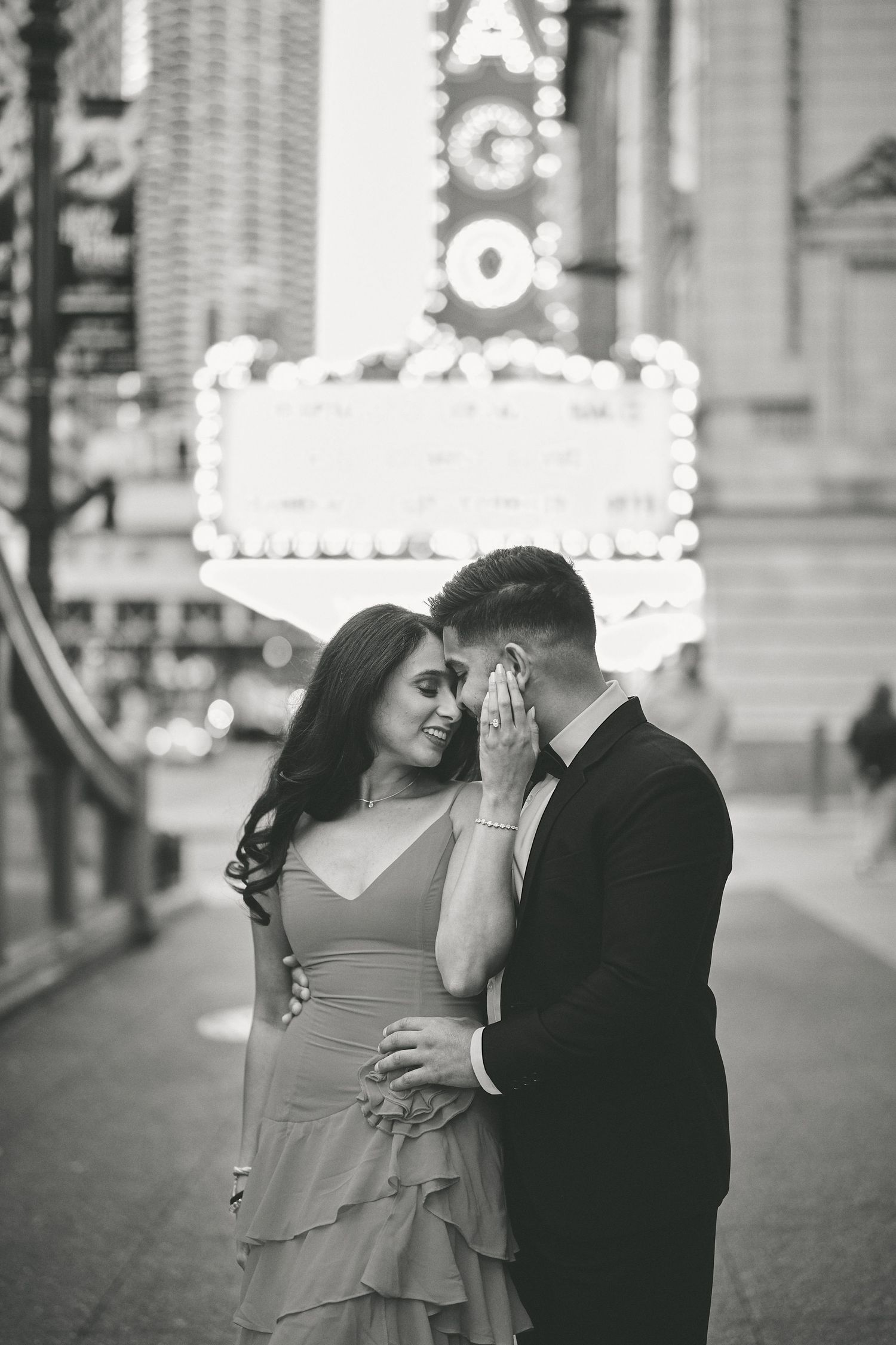 A romantic black and white photo of a couple sharing an intimate moment in front of the Chicago Theatre marquee.