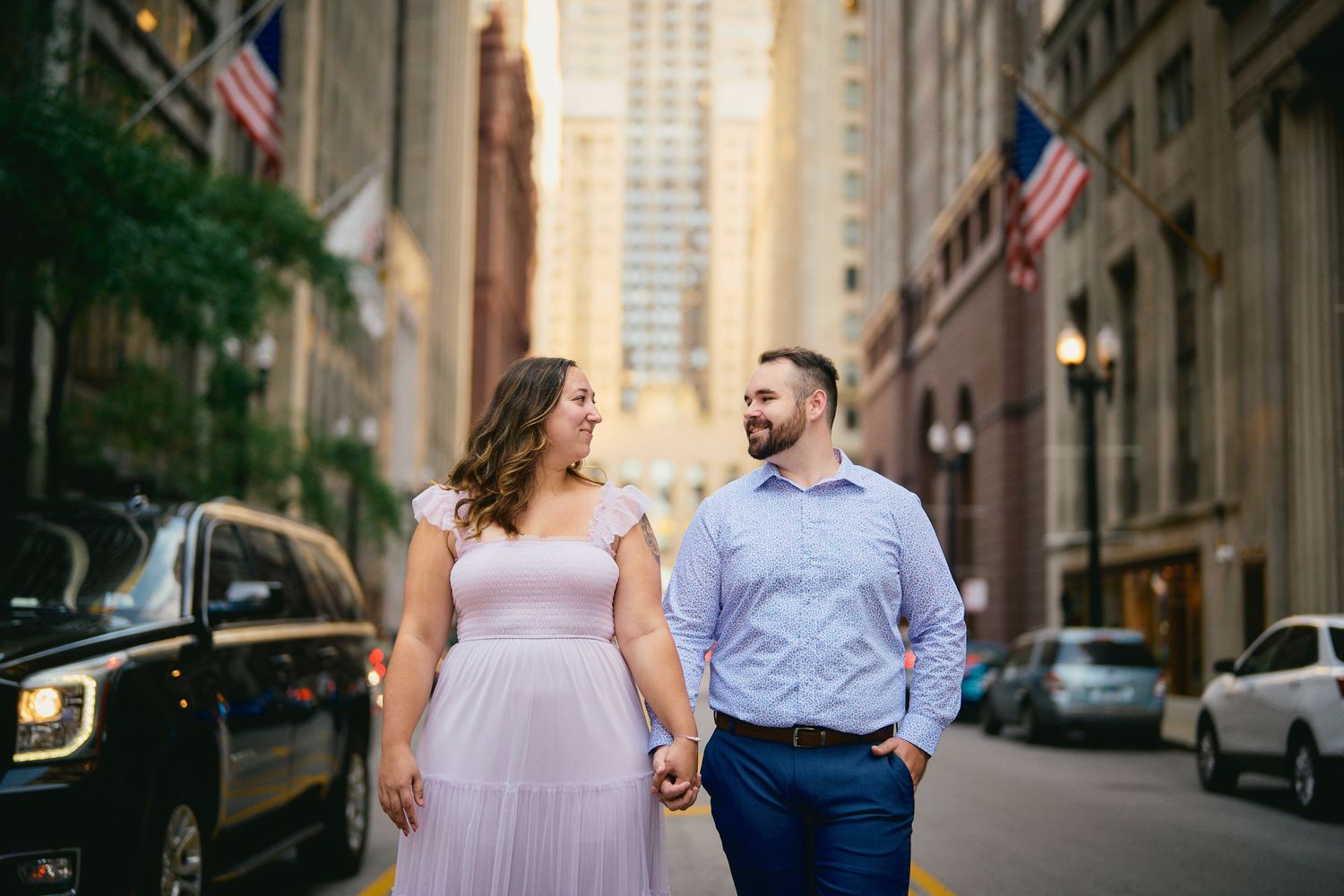 A couple walking and smiling together on a downtown street with tall buildings and American flags in Chicago.