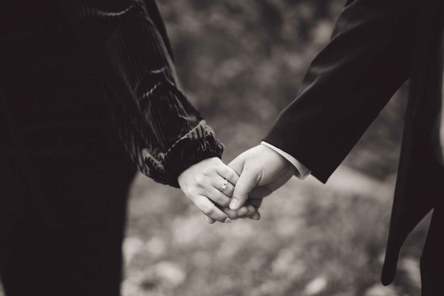 A black and white close-up photo of two people holding hands together in a romantic gesture.