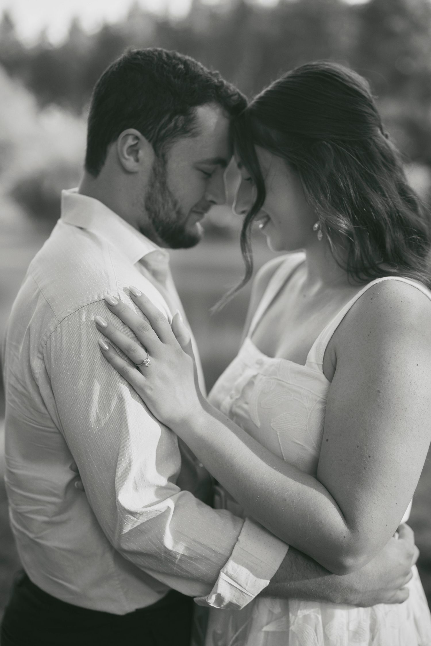 A romantic black and white portrait of a couple in an intimate embrace outdoors with soft natural lighting.