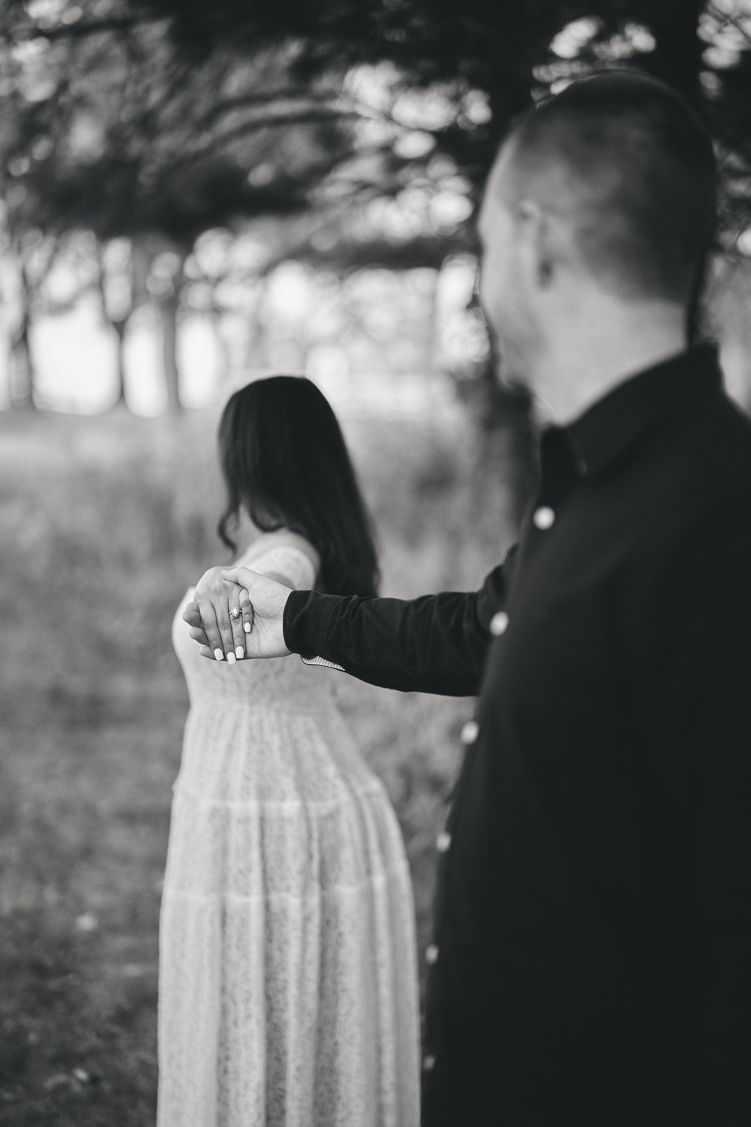Black and white romantic photo of two people in an outdoor setting with soft bokeh lighting.
