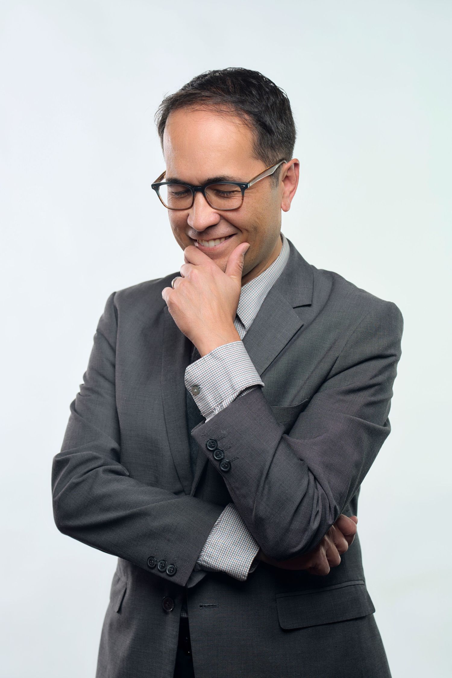 Professional portrait of person in grey suit and glasses with contemplative expression.