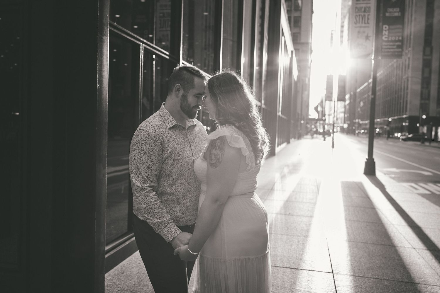 Two people share a romantic moment on a city sidewalk at sunset as golden light streams down the street.