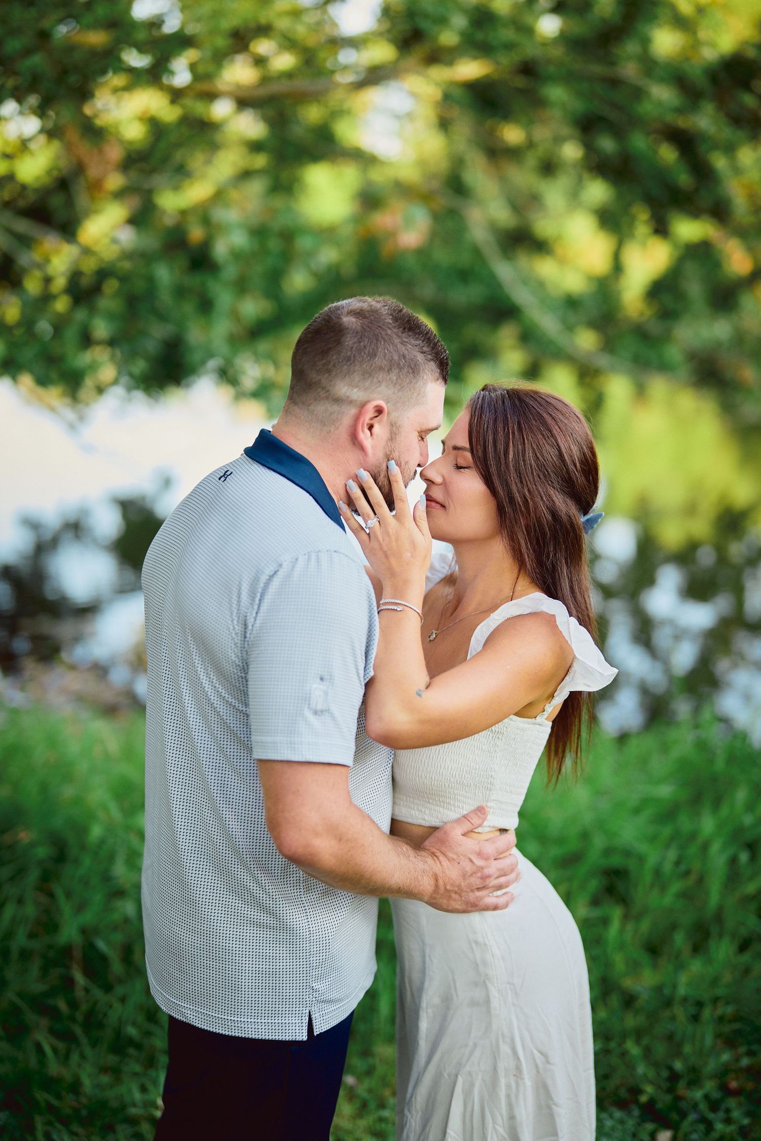 An intimate moment between a couple sharing a tender embrace against a backdrop of summer foliage.
