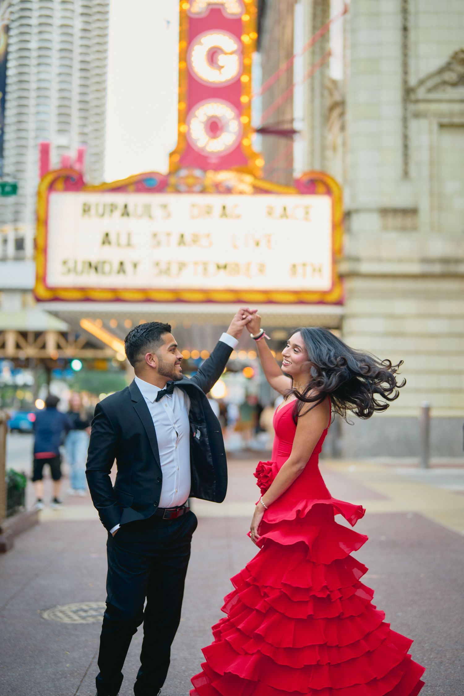 A couple dances joyfully outside the Chicago Theater, with the woman wearing a stunning red ruffled gown.