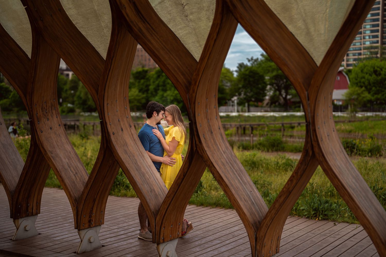A couple shares a romantic moment viewed through a wooden architectural lattice on an outdoor walkway.