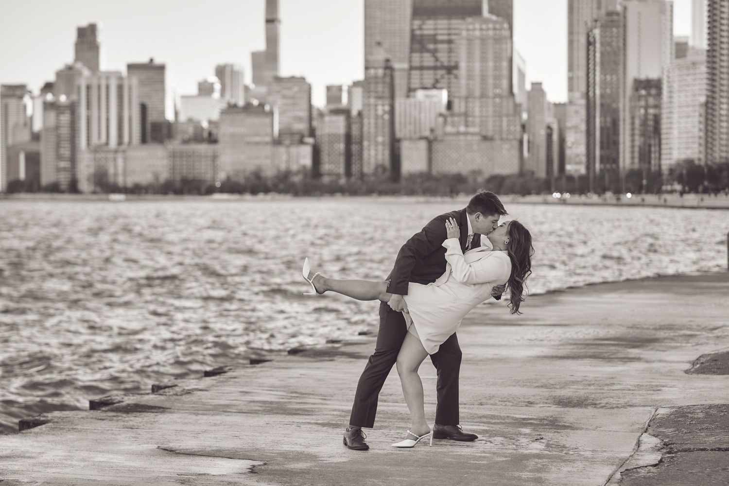 A romantic couple embraces in a dip pose along the waterfront with the Chicago skyline in black and white.