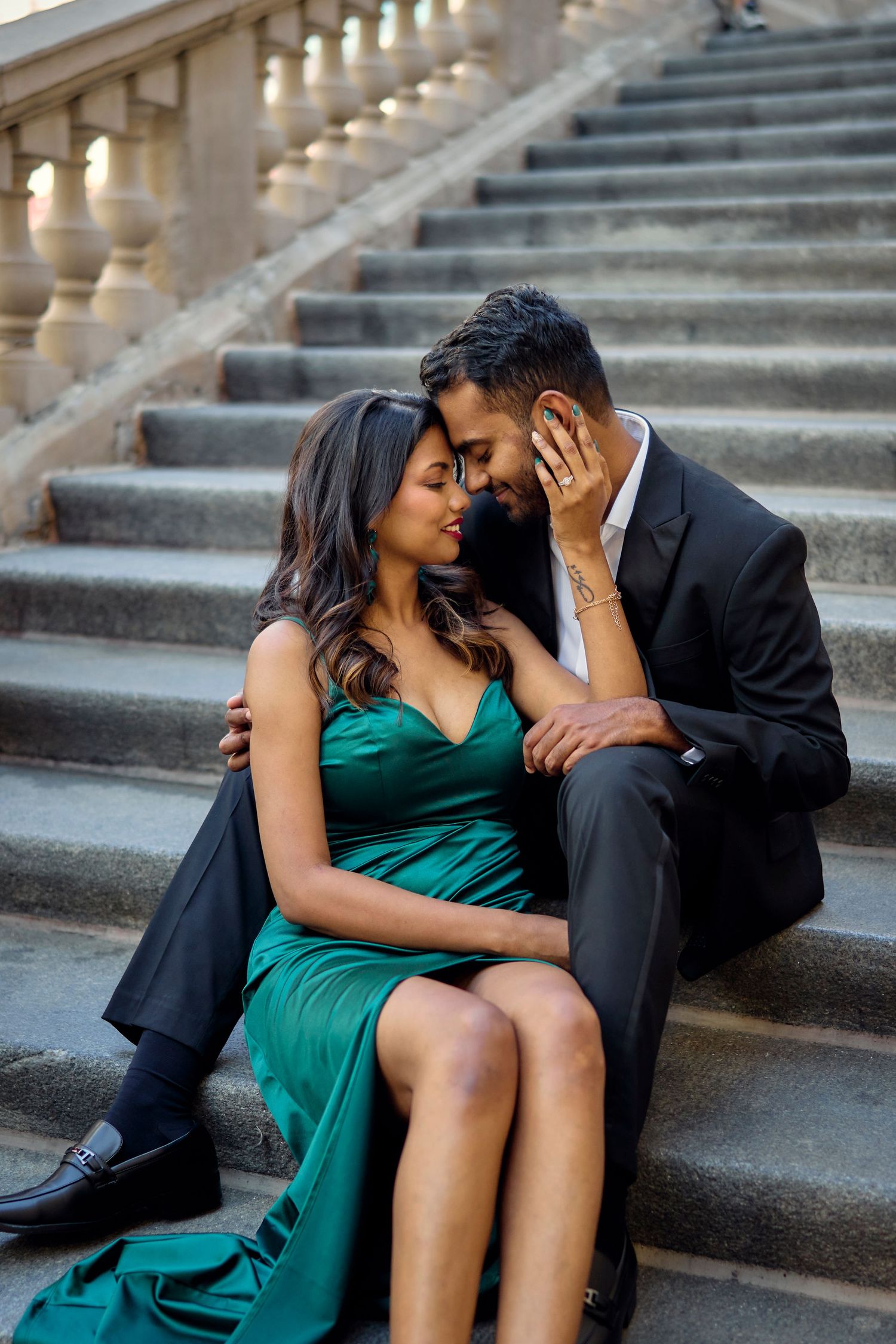 A romantic couple in formal attire sharing an intimate moment on elegant stone steps with warm lighting above.