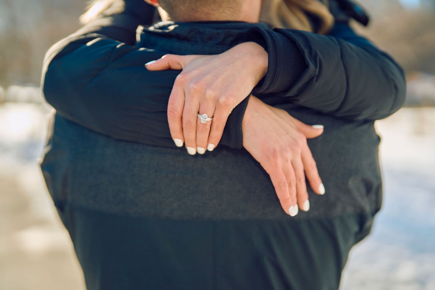 Close up of hands showing engagement ring in winter setting with snowy background.