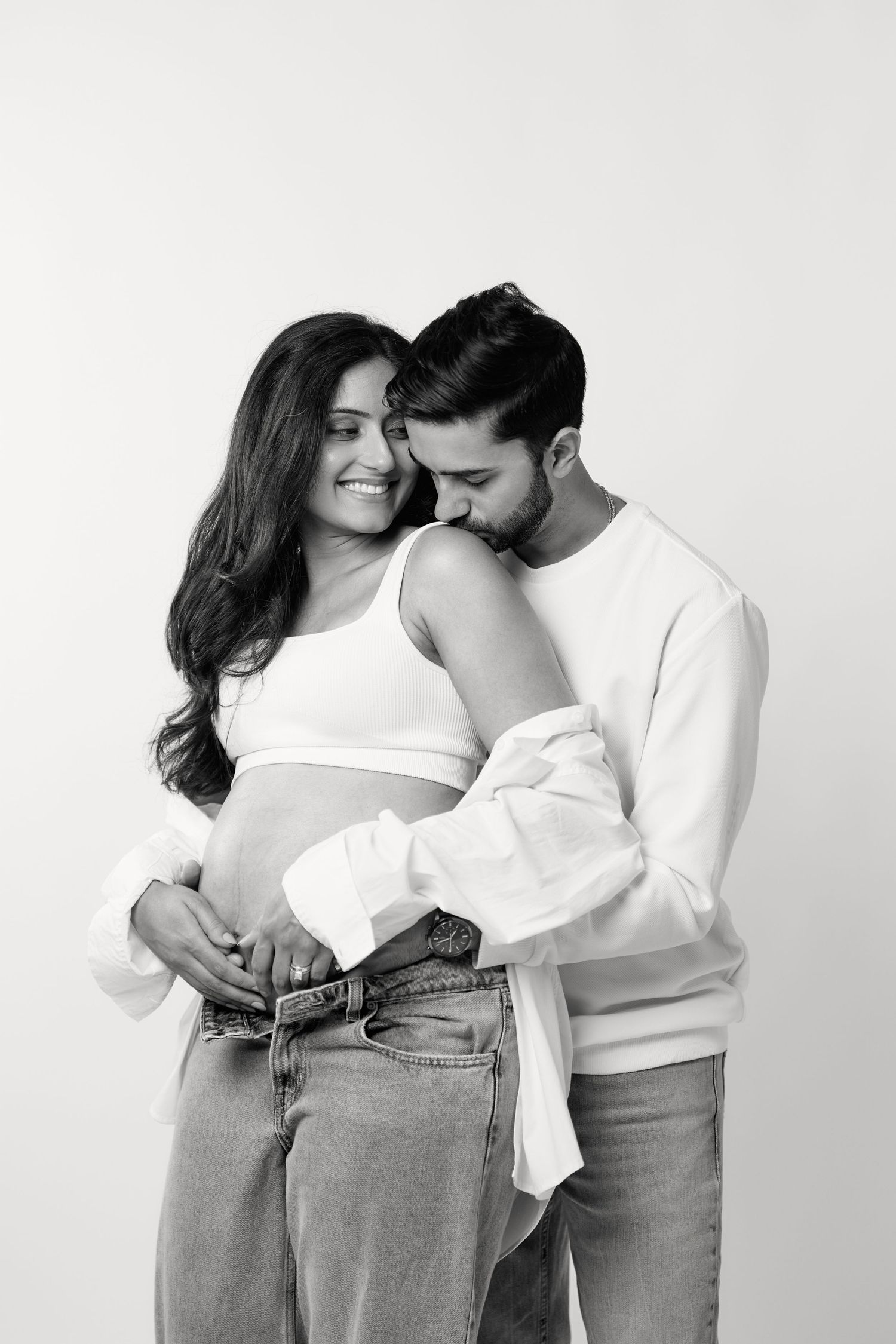 A romantic black and white portrait of a couple embracing, with the woman wearing a white crop top and jeans.