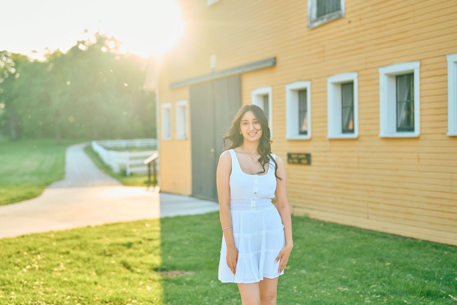 A figure stands in front of a yellow building on a sunny evening with golden sunlight shining through trees.