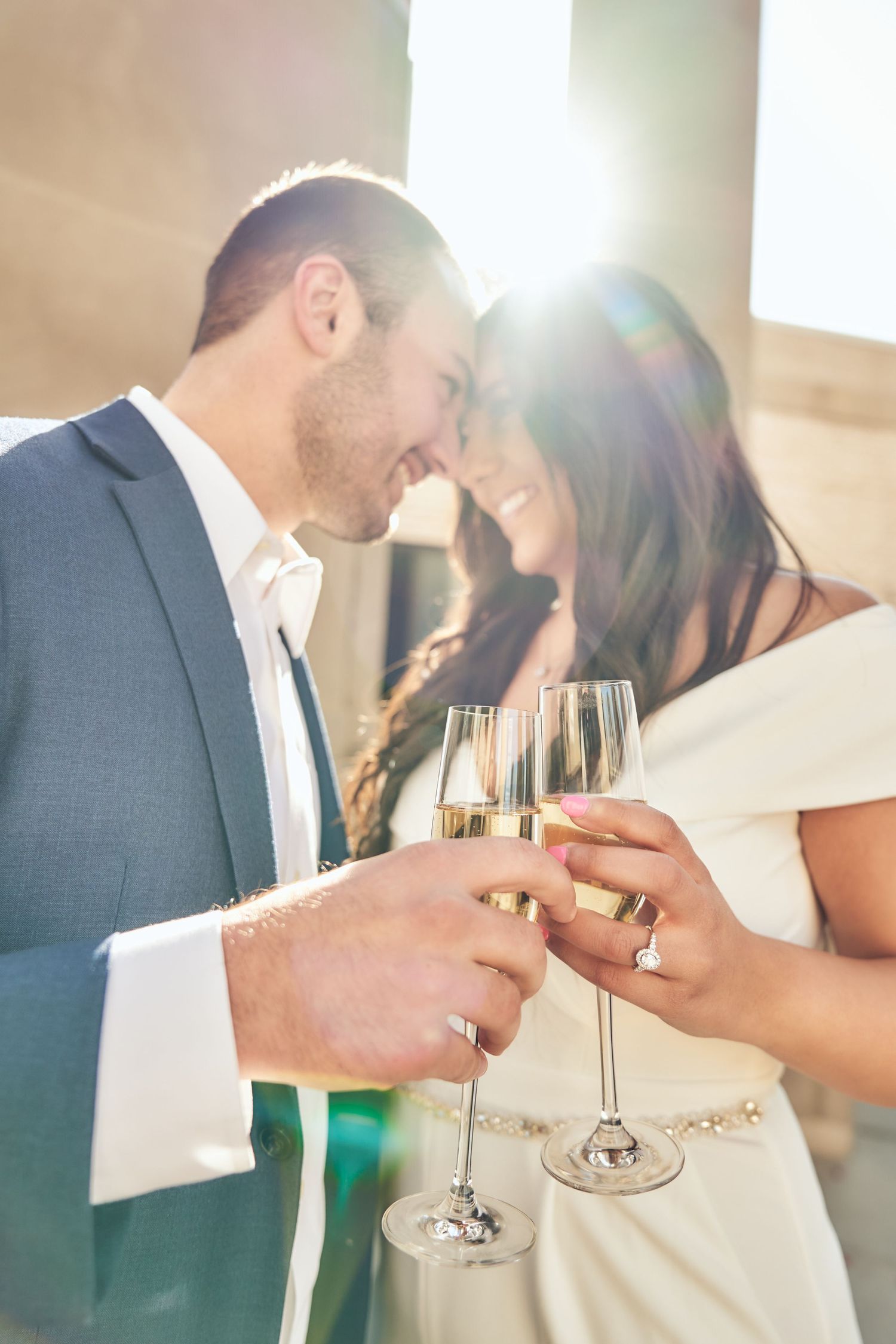 A romantic moment between a couple toasting with champagne glasses during a wedding celebration in sunlit setting.