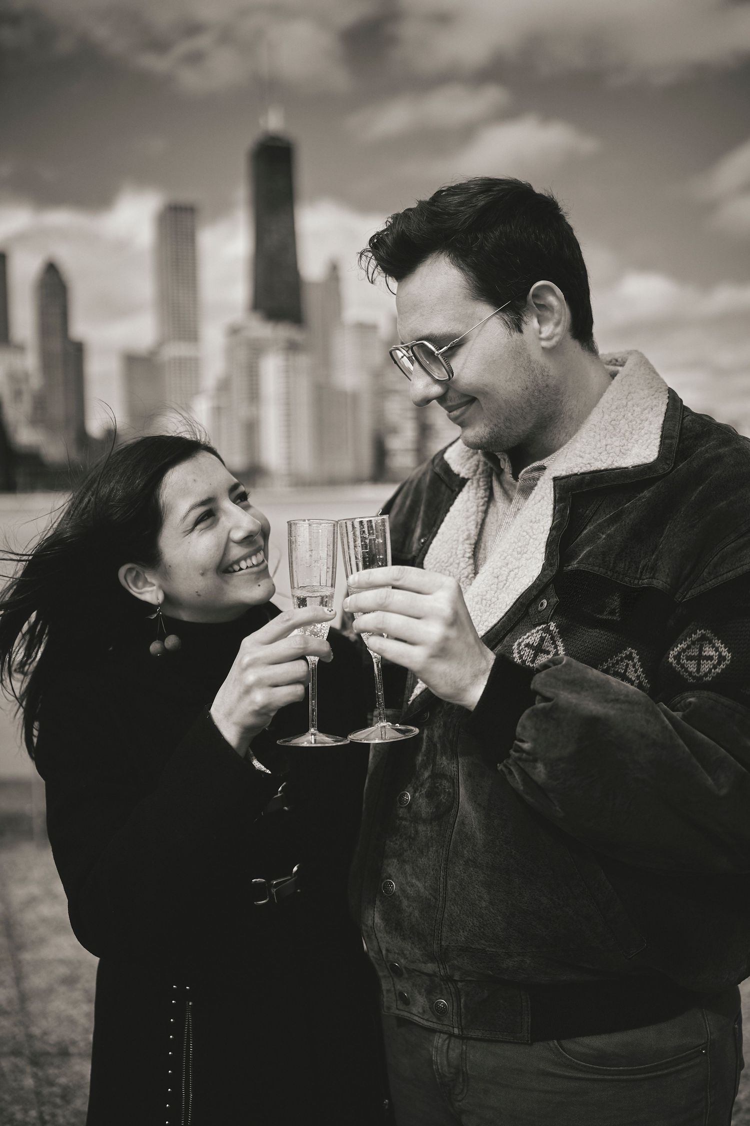 A couple toasts with wine glasses against a dramatic city skyline in black and white photography.