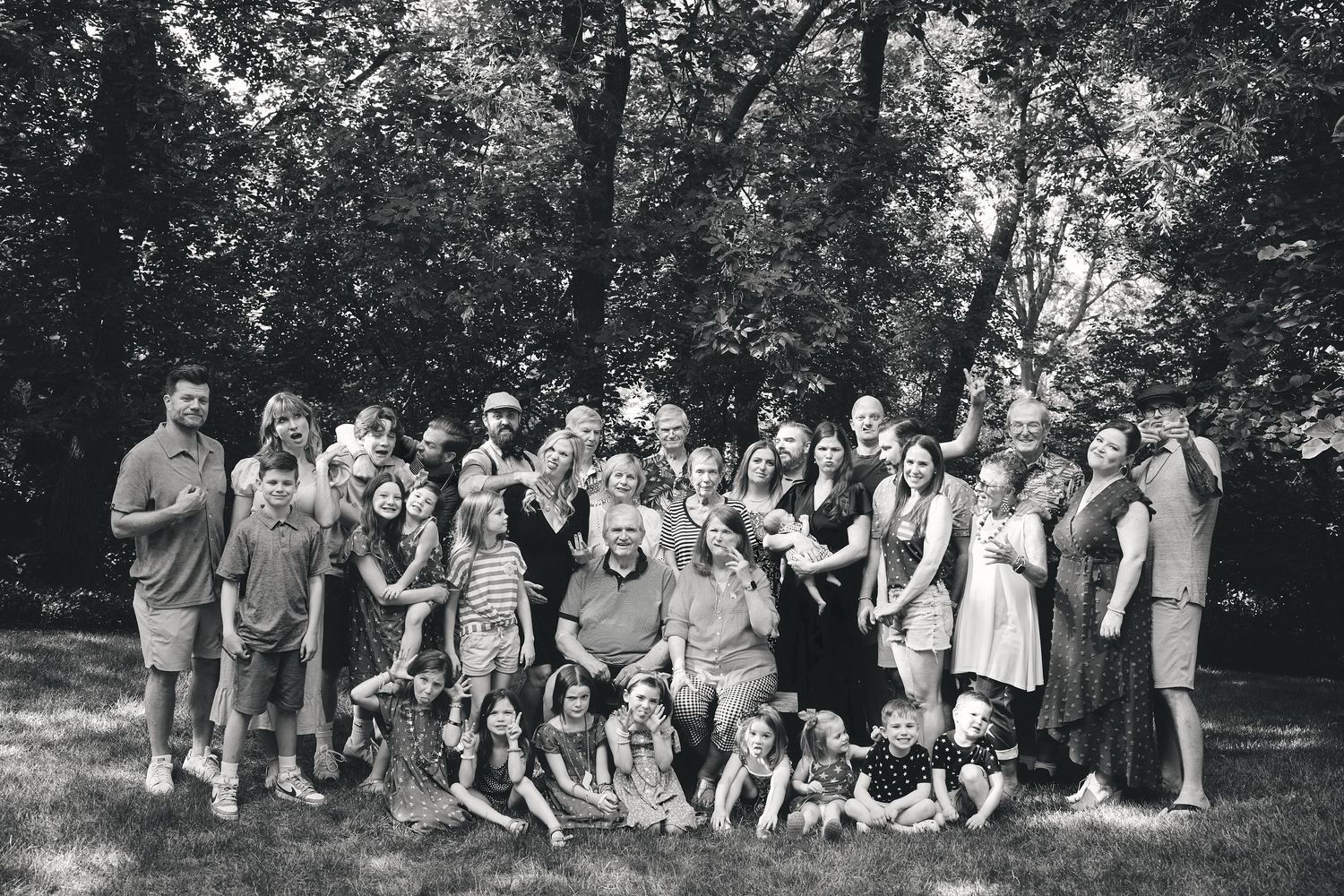 A large group poses together outdoors for a casual black and white photo in a wooded area.