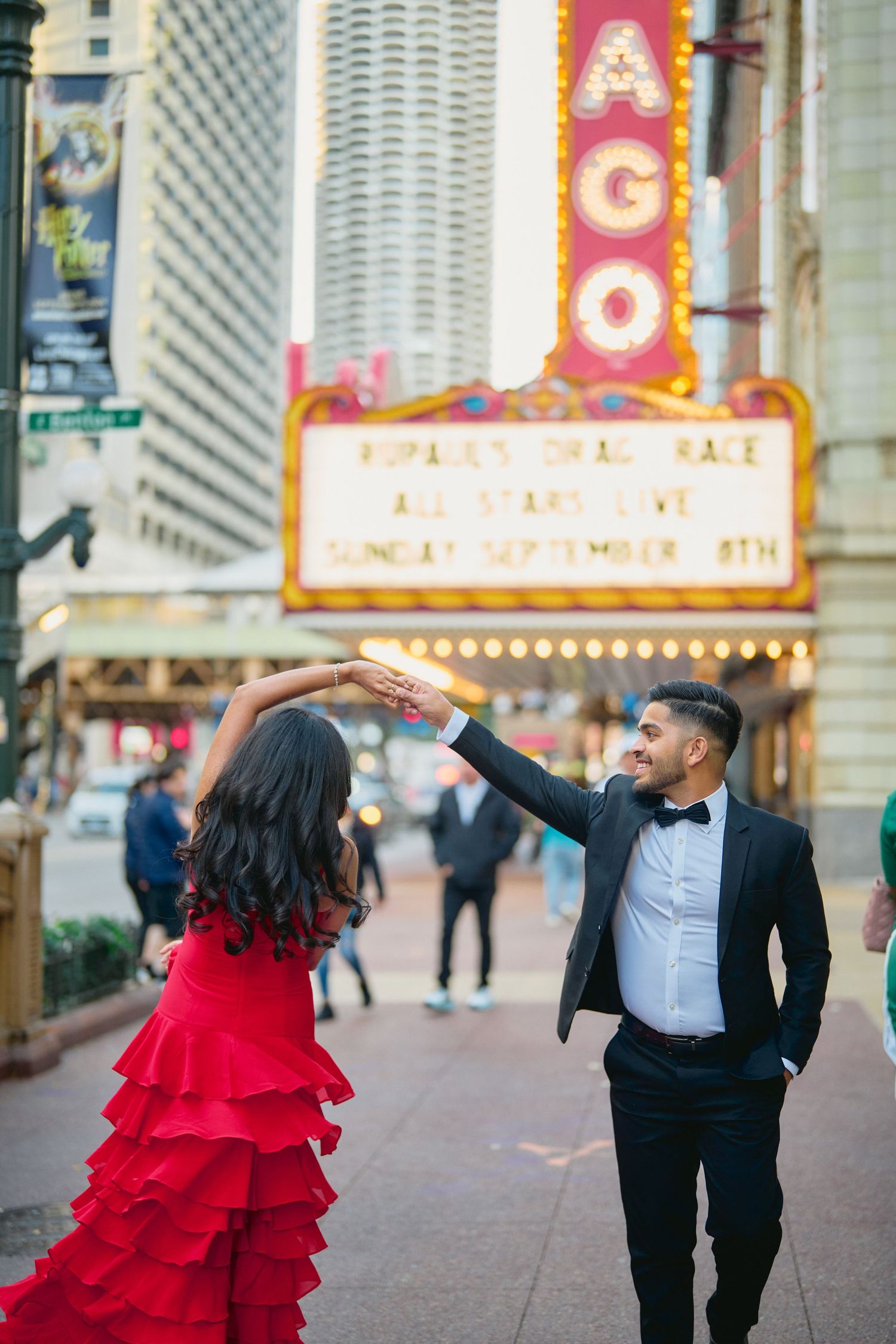 A couple dances on the sidewalk in front of the iconic Chicago Theater, with the woman wearing a flowing red dress.