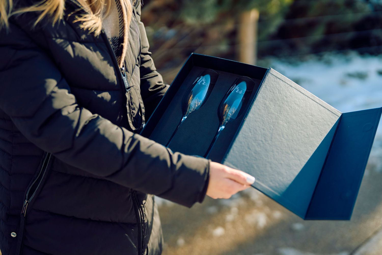 Someone holds a blue winter glove display box outside in winter environment.