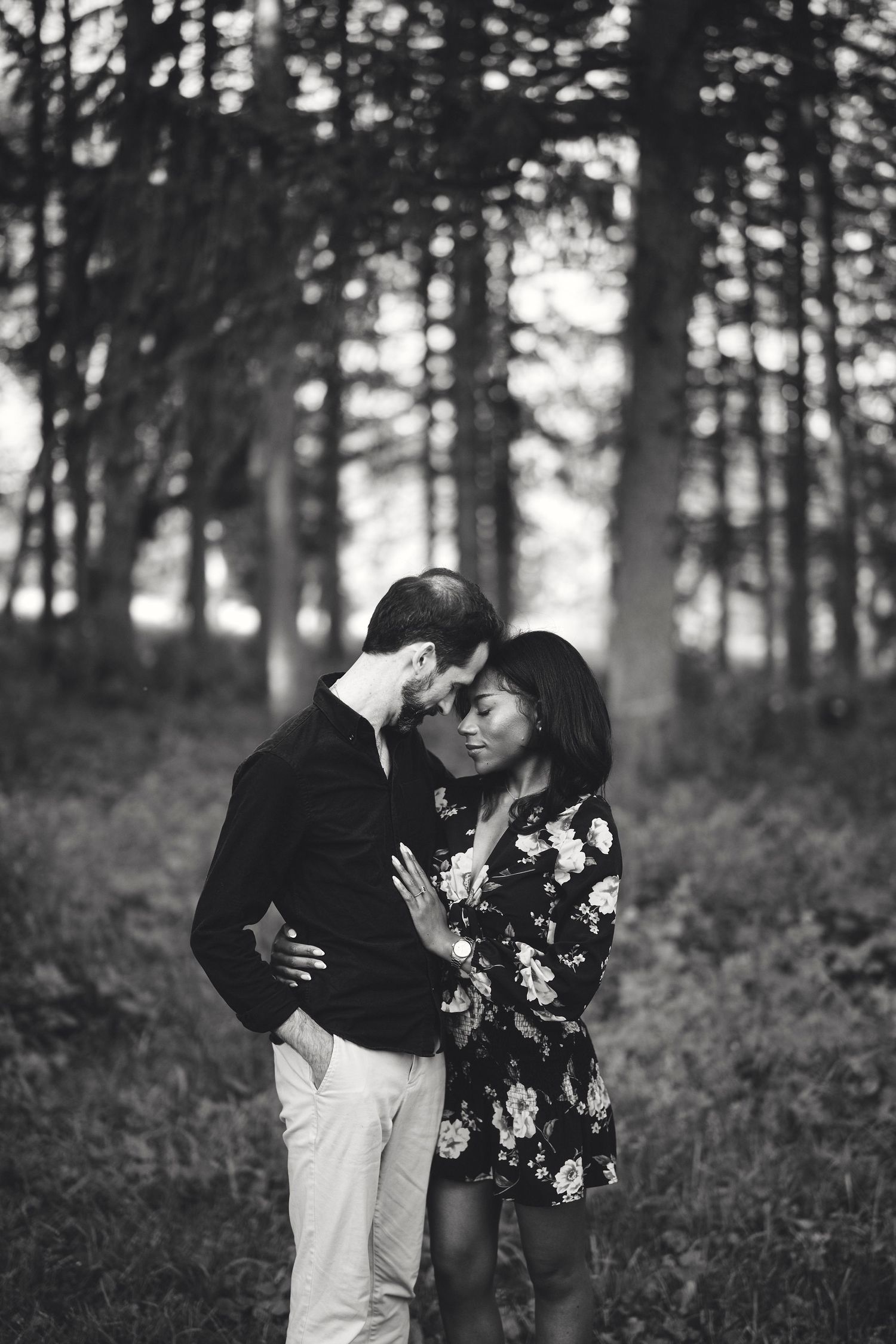 A romantic black and white portrait of a couple embracing in a misty forest setting with sunlight filtering through trees.