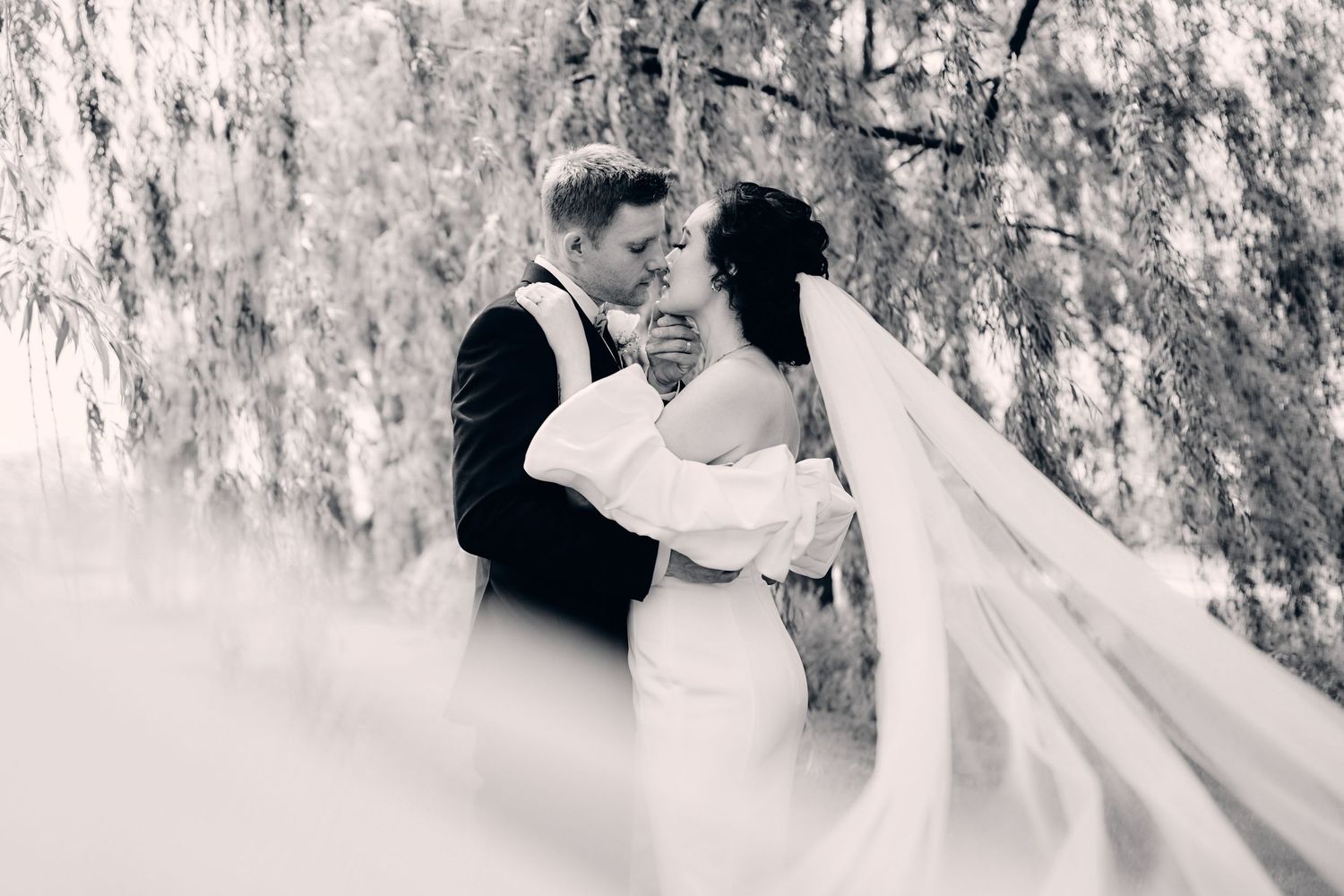 Black and white wedding portrait with flowing veil creating ethereal romantic atmosphere.