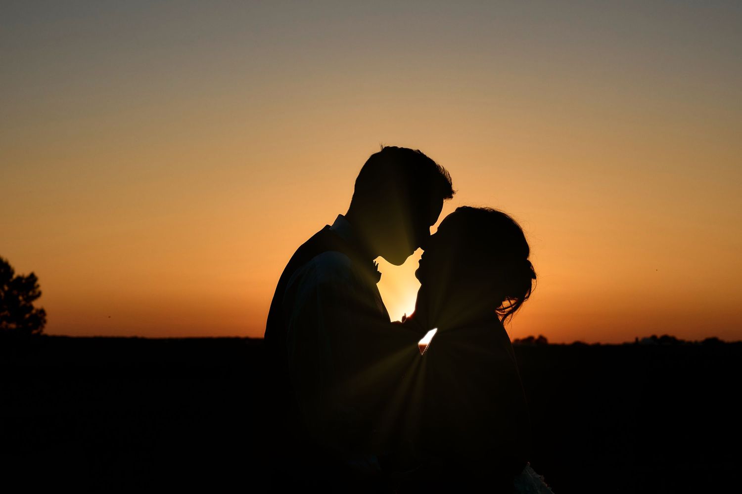 Silhouetted couple in tender embrace against a dramatic sunset sky.