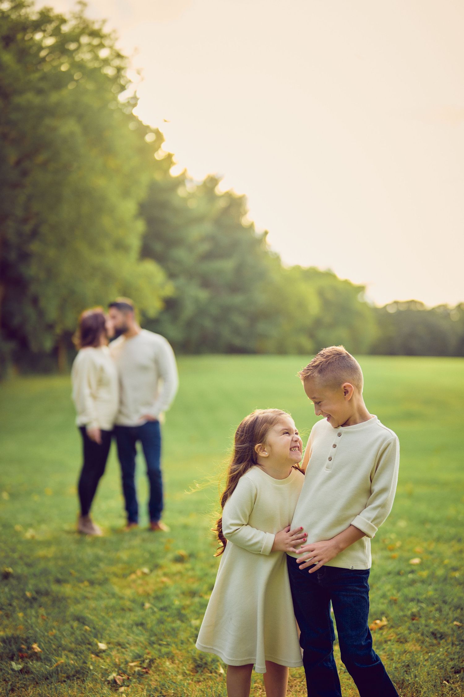 Family portrait in a sunlit meadow with children in foreground and parents in background.