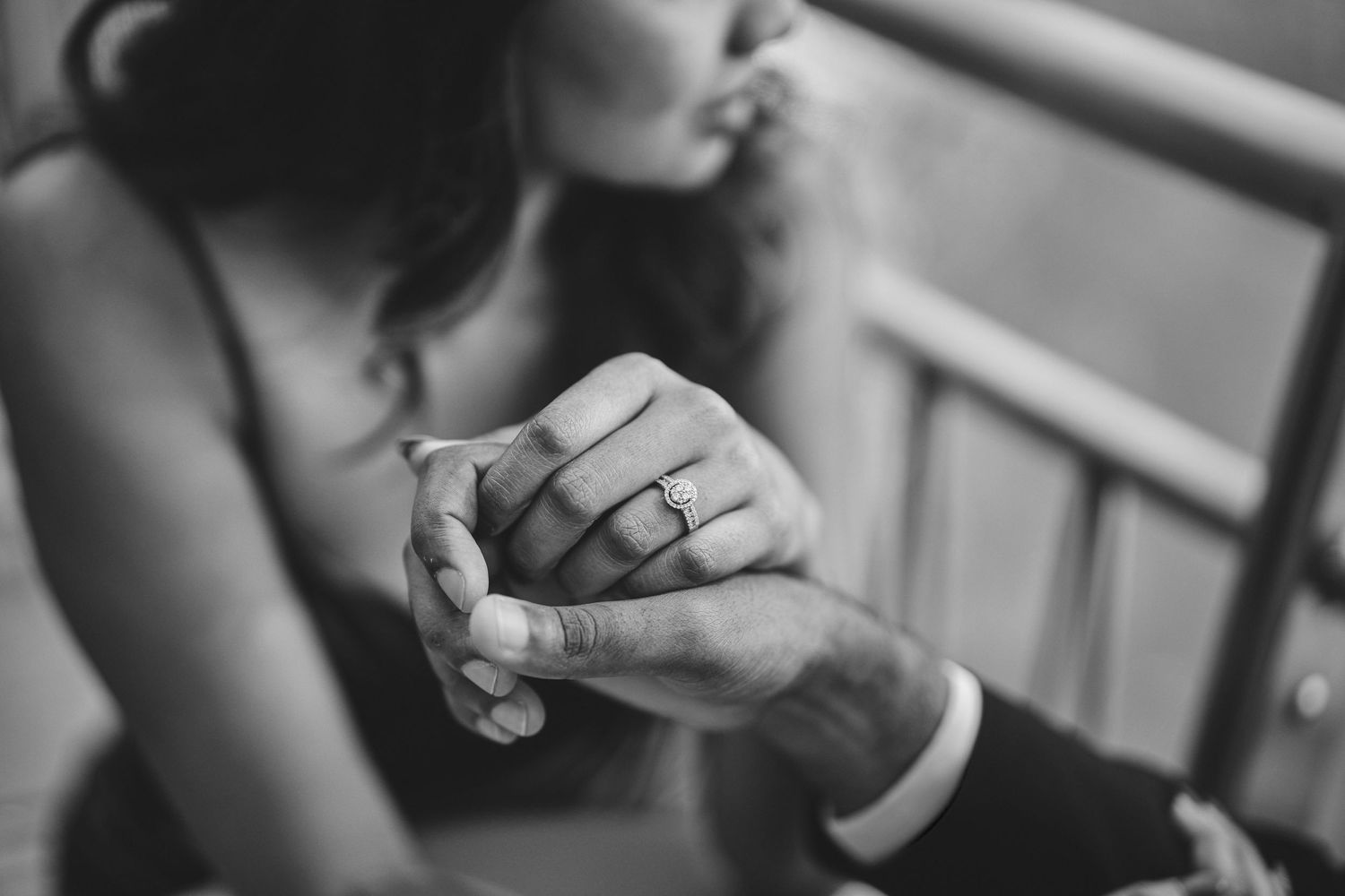 Close-up black and white photo of clasped hands with a ring.
