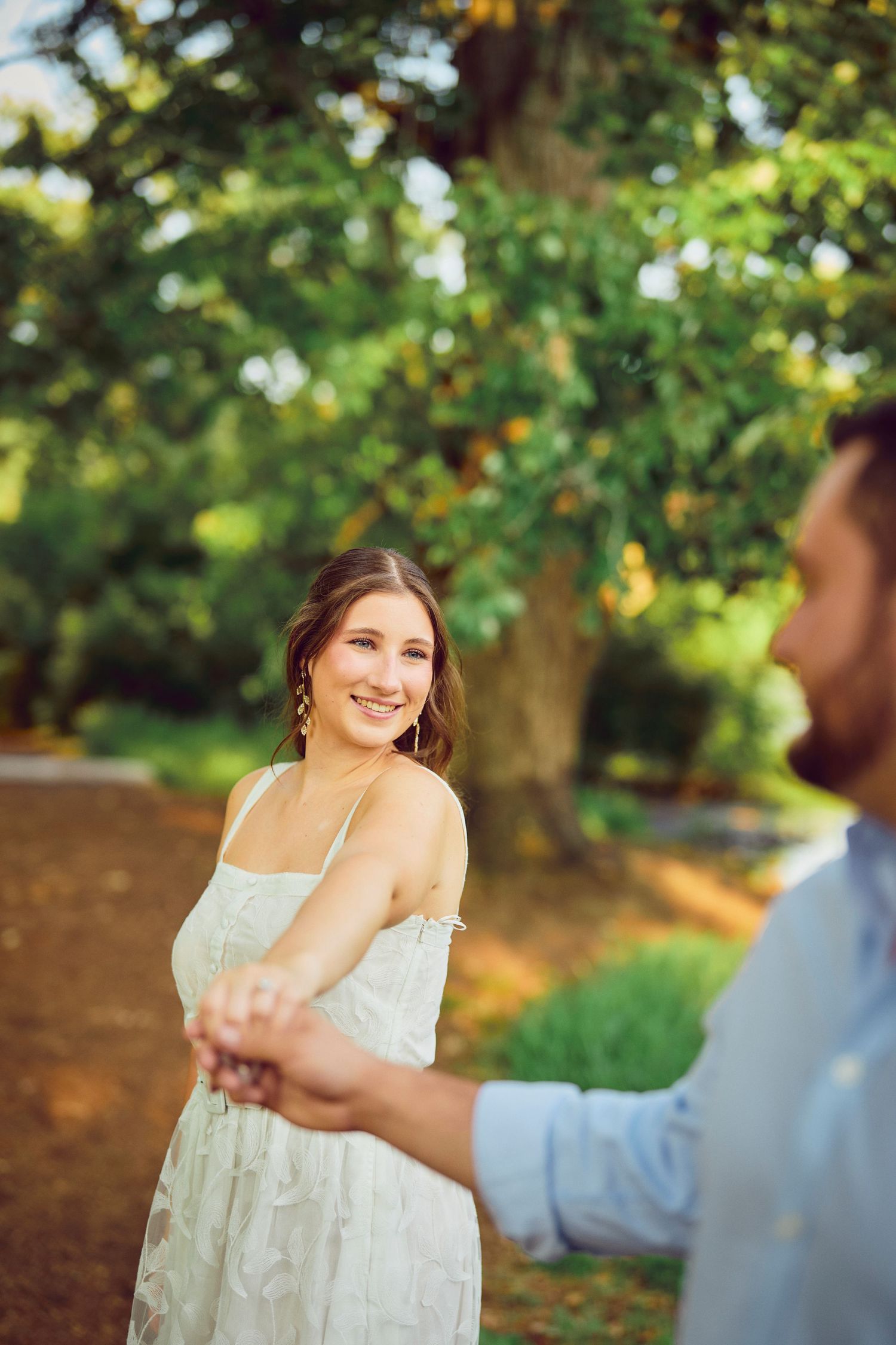 Couple holding hands in a romantic garden setting with sunlit greenery in the background.