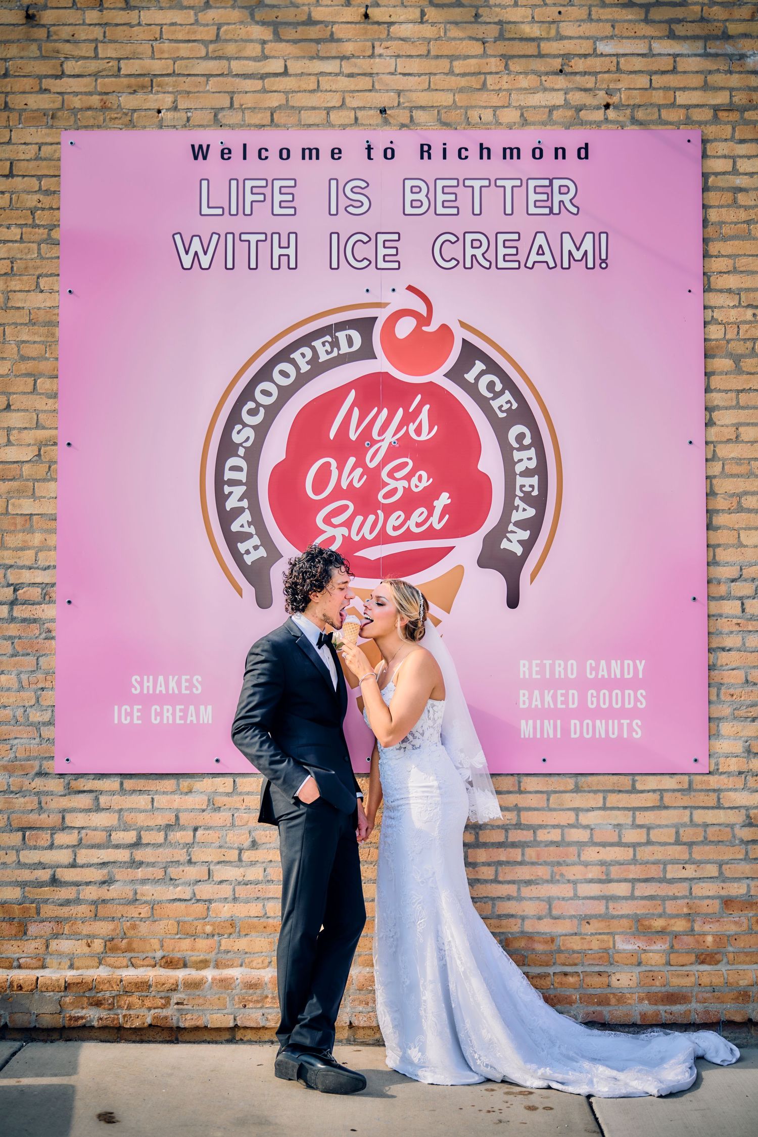 A couple in wedding attire poses against a pink wall with a vintage Wy's Ice Cream shop sign in Richmond.