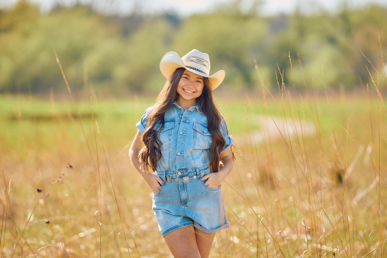 Casual western style outfit featuring denim romper and cowboy hat in a golden field at sunset.