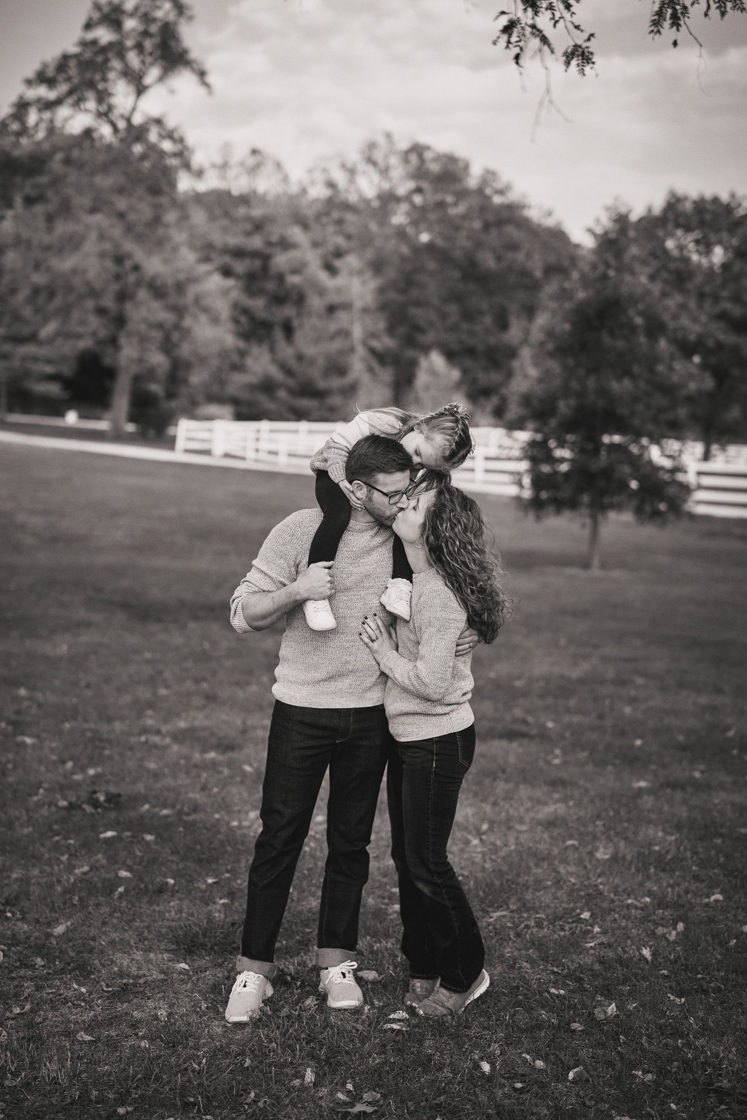 Black and white romantic portrait of couple embracing outdoors near white fence.