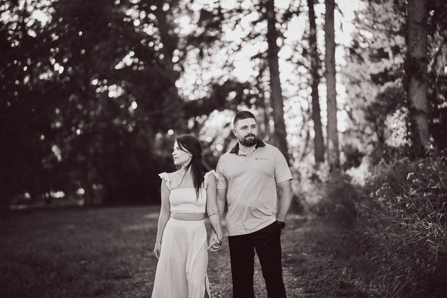A romantic couple poses together in a forest setting with soft black and white tones.