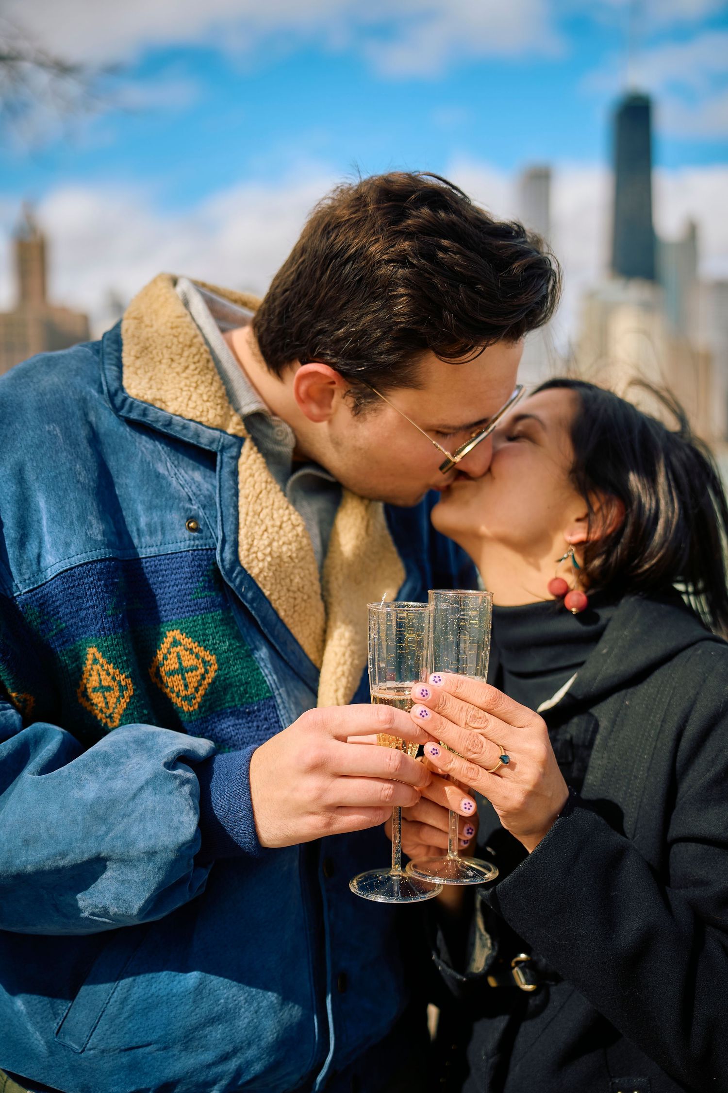 Couple sharing a romantic champagne toast and kiss against a city skyline backdrop.