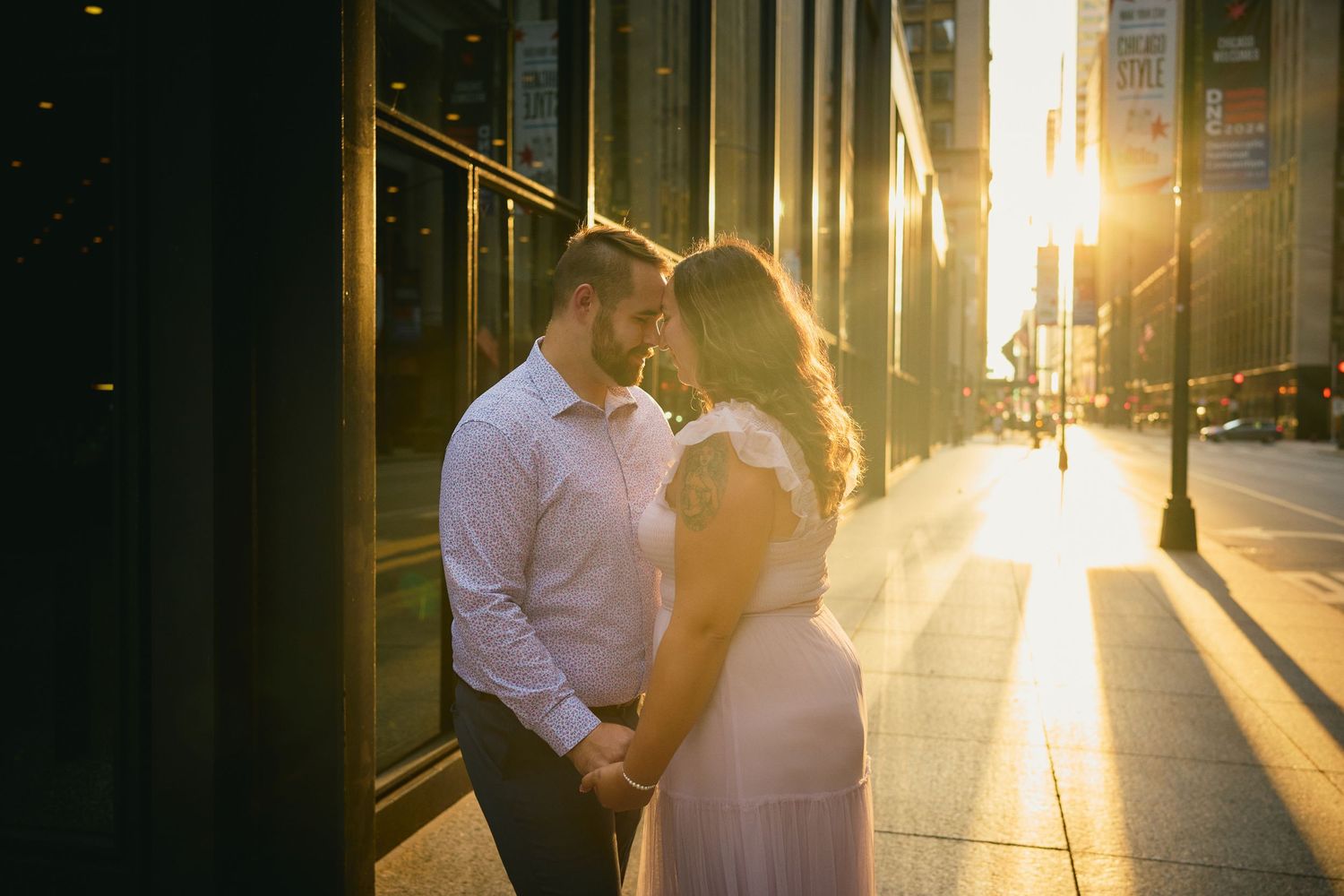 A couple shares a romantic moment in a city street at golden hour as sunlight streams between buildings.