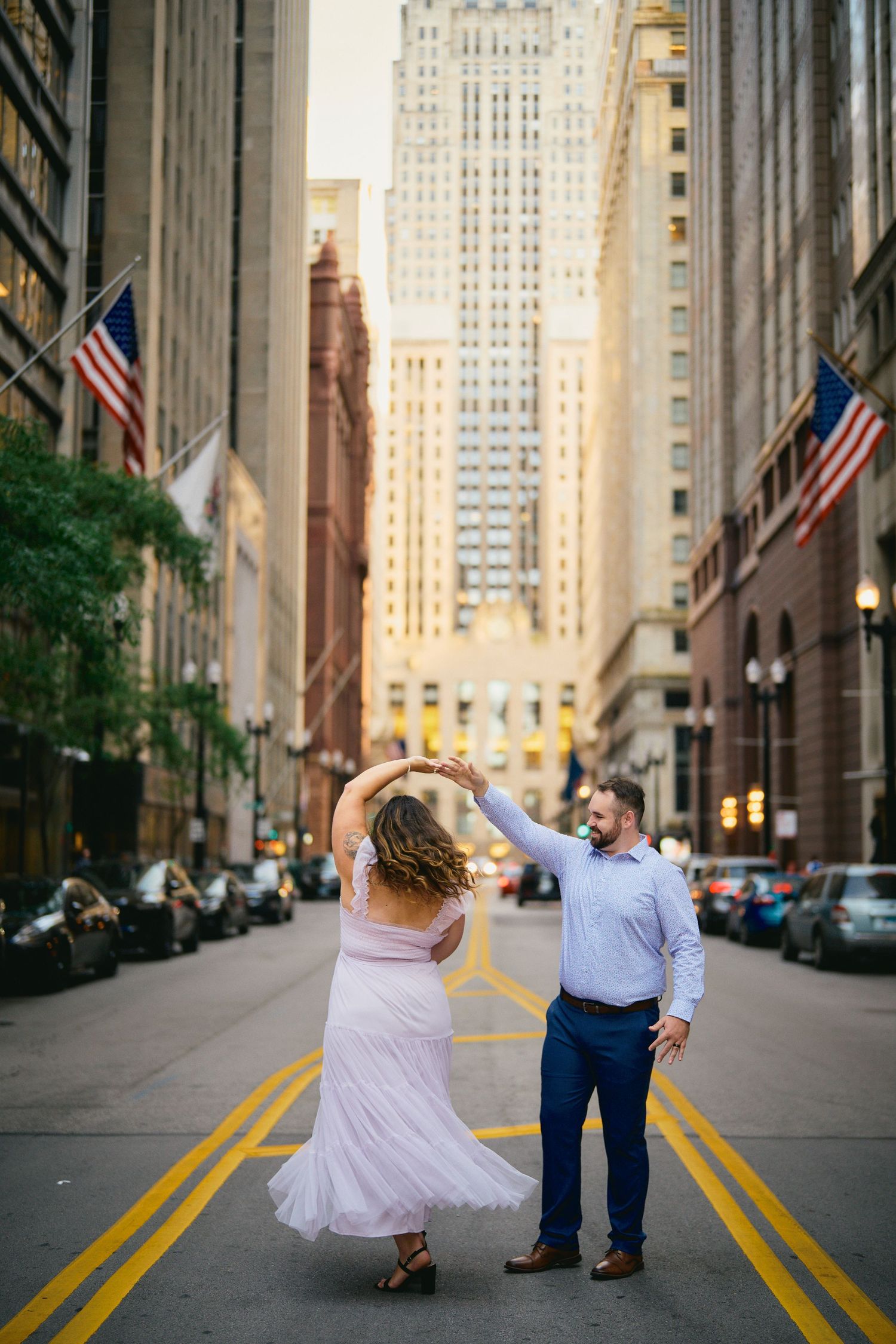 A couple dances in the middle of a Chicago street lined with American flags and tall buildings.