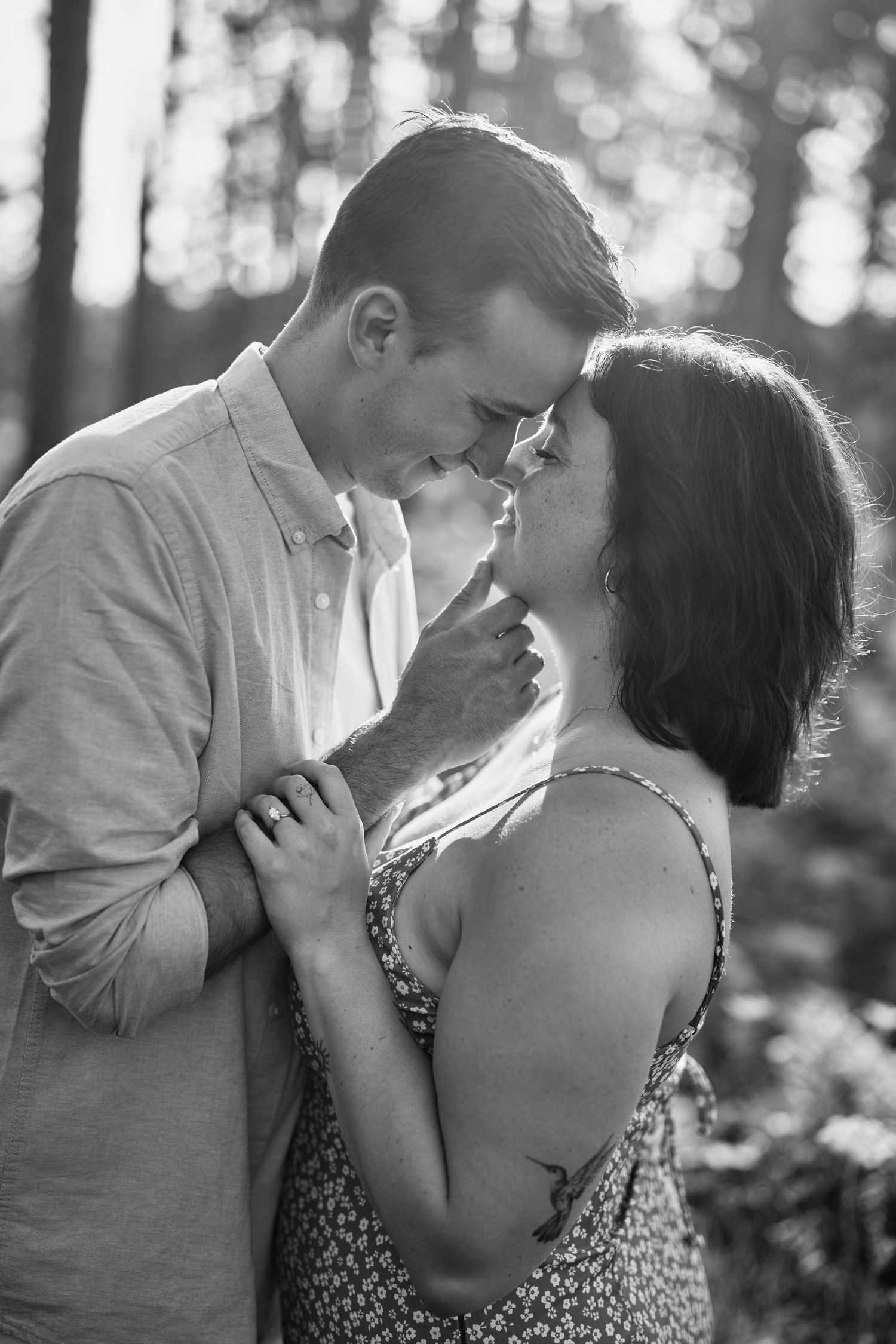 A romantic black and white photo of a couple sharing an intimate moment in a sunlit forest setting.