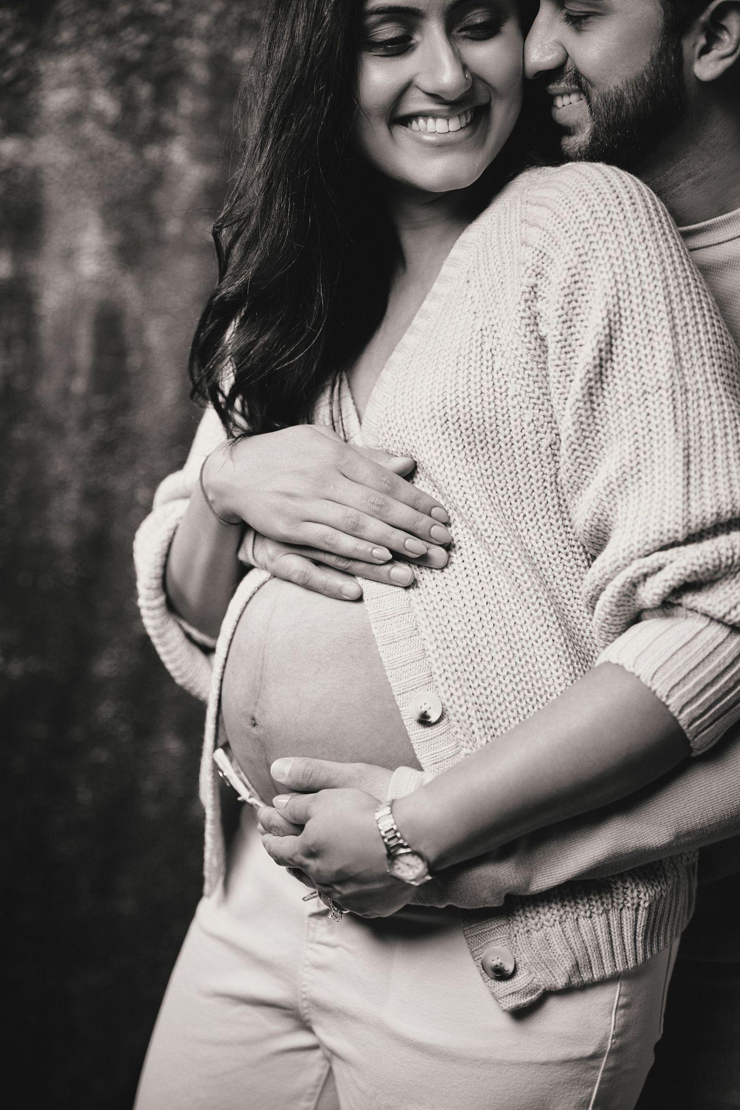 A couple embraces tenderly during a maternity photoshoot, with hands lovingly placed on the pregnant belly.