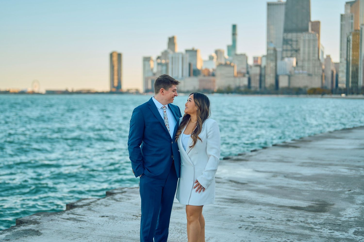 A couple shares a romantic moment along Lake Michigan with Chicago's skyline in the background at sunset.