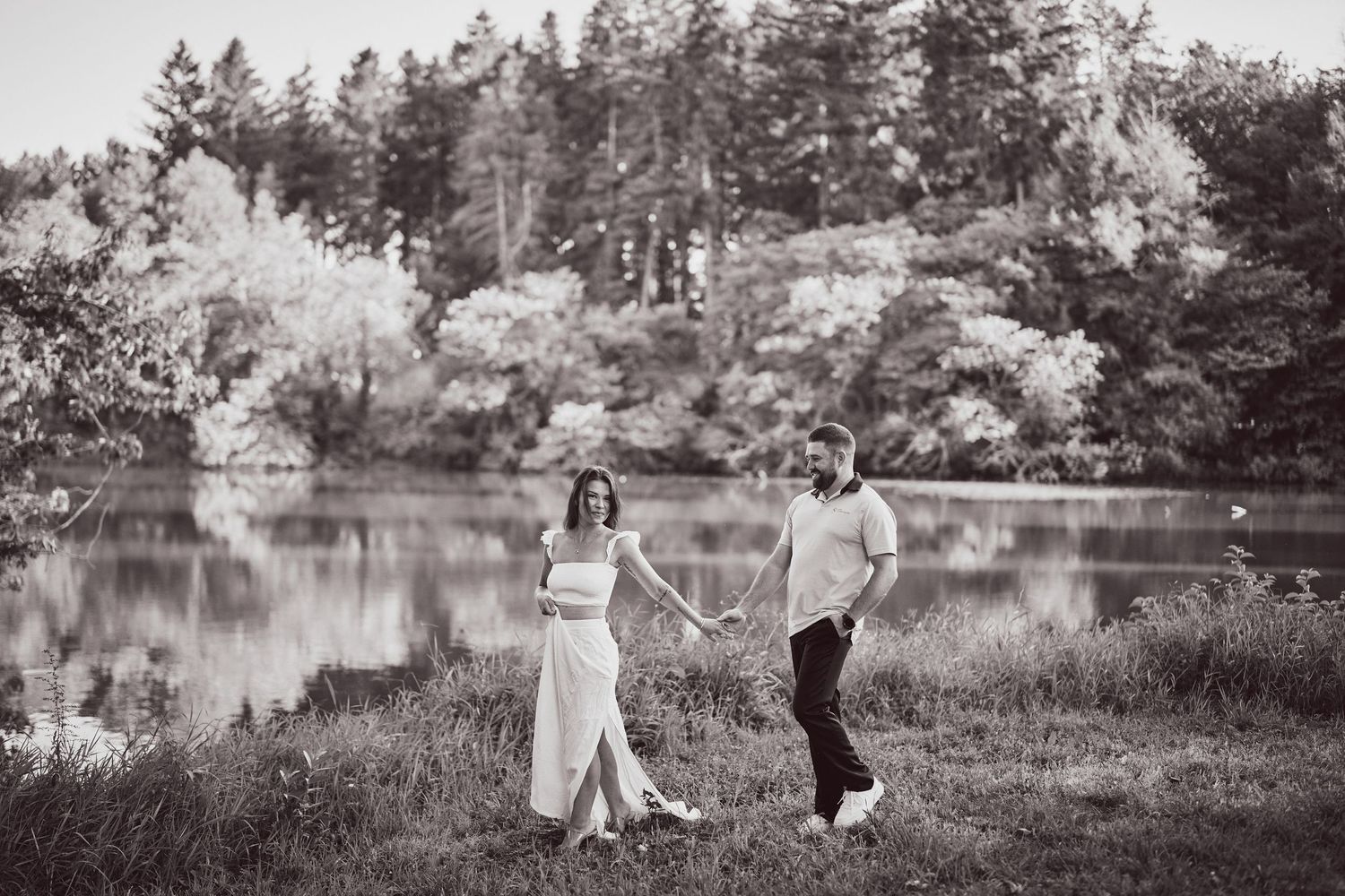 Black and white romantic scene of a couple dancing together by a serene lake surrounded by flowering trees.